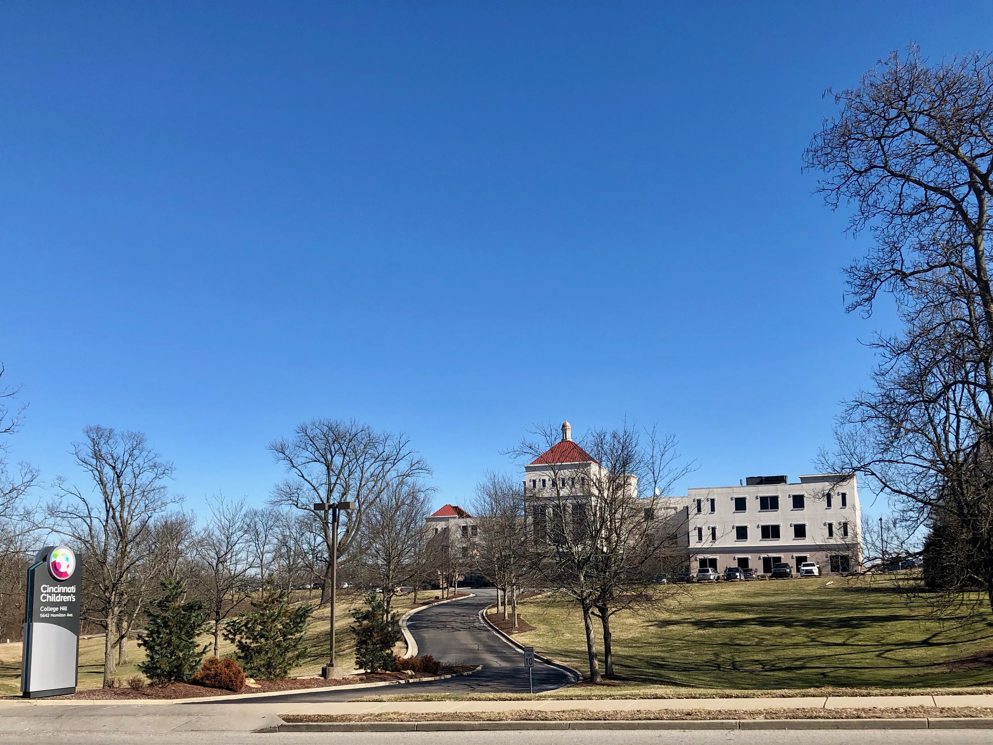 Hospital sign post in front of a domed brick building and a newer multi-story building on a clear day.