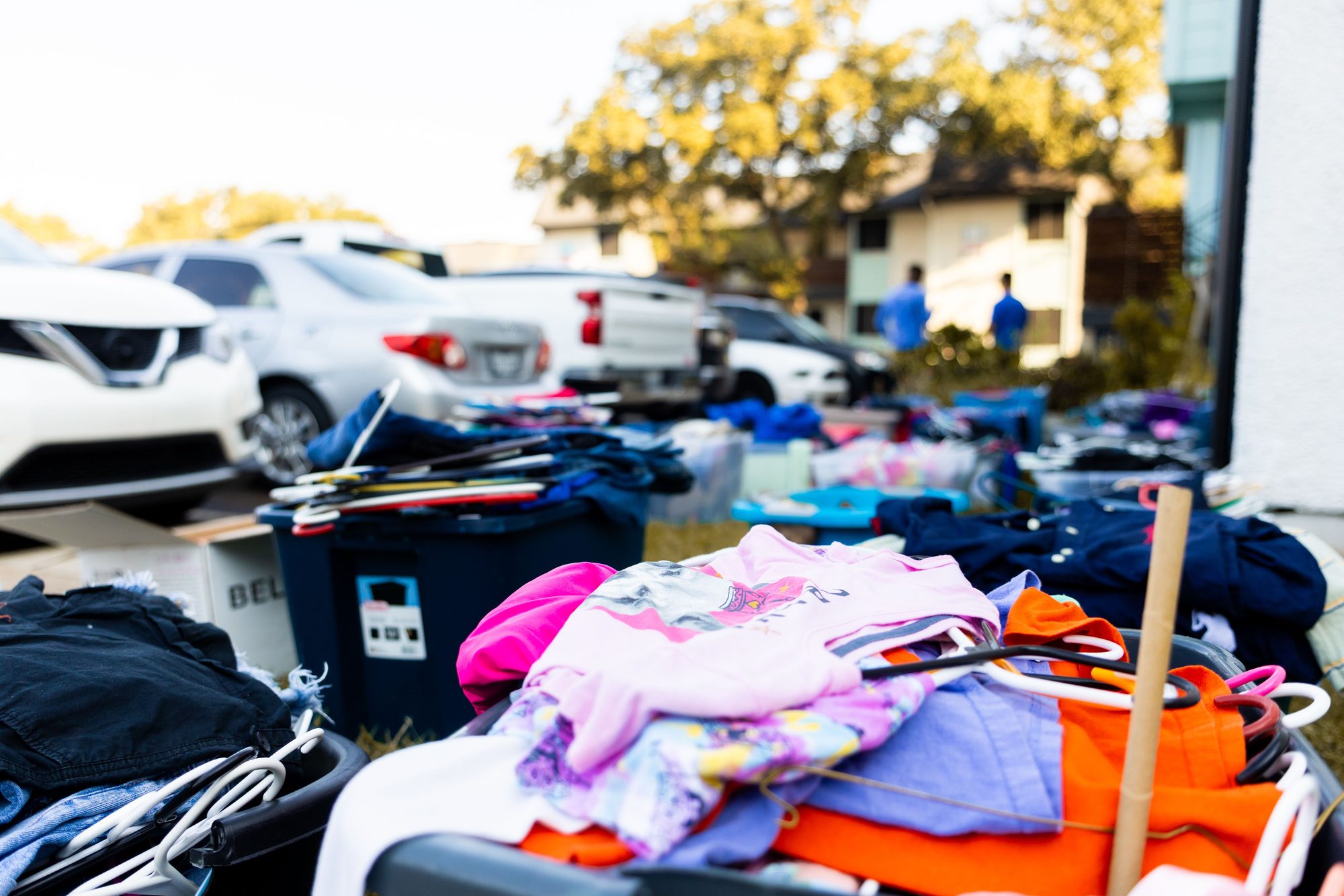 An outdoor garage sale featuring various clothes and cars in a suburban setting.