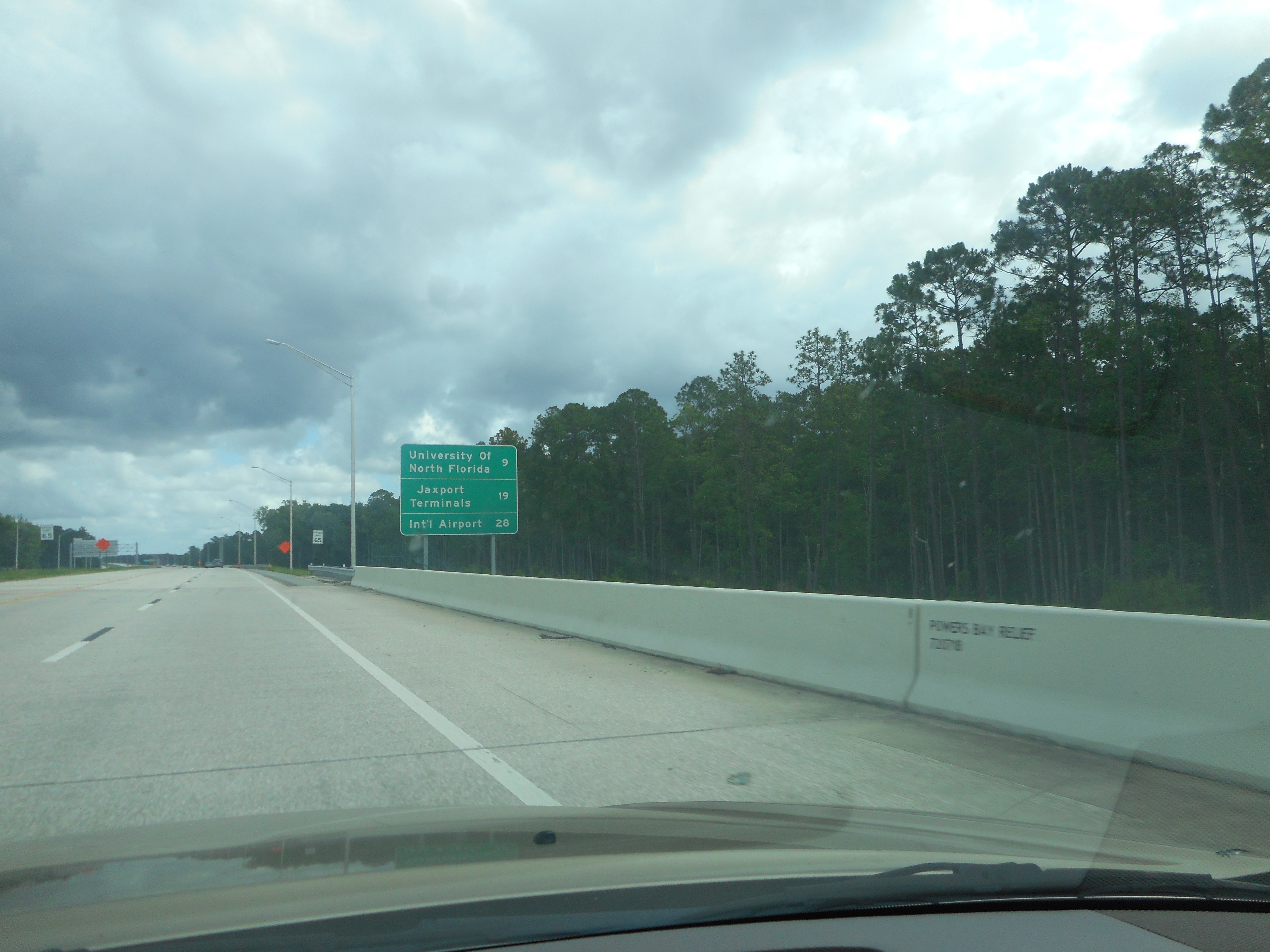 Green overhead highway sign directing traffic toward an international airport.