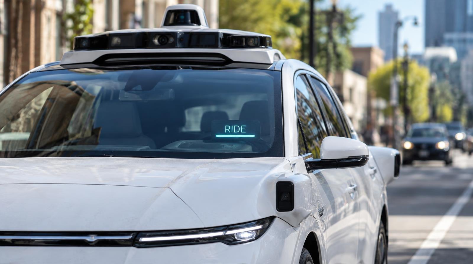 White autonomous electric vehicle with roof sensors driving on a city street.