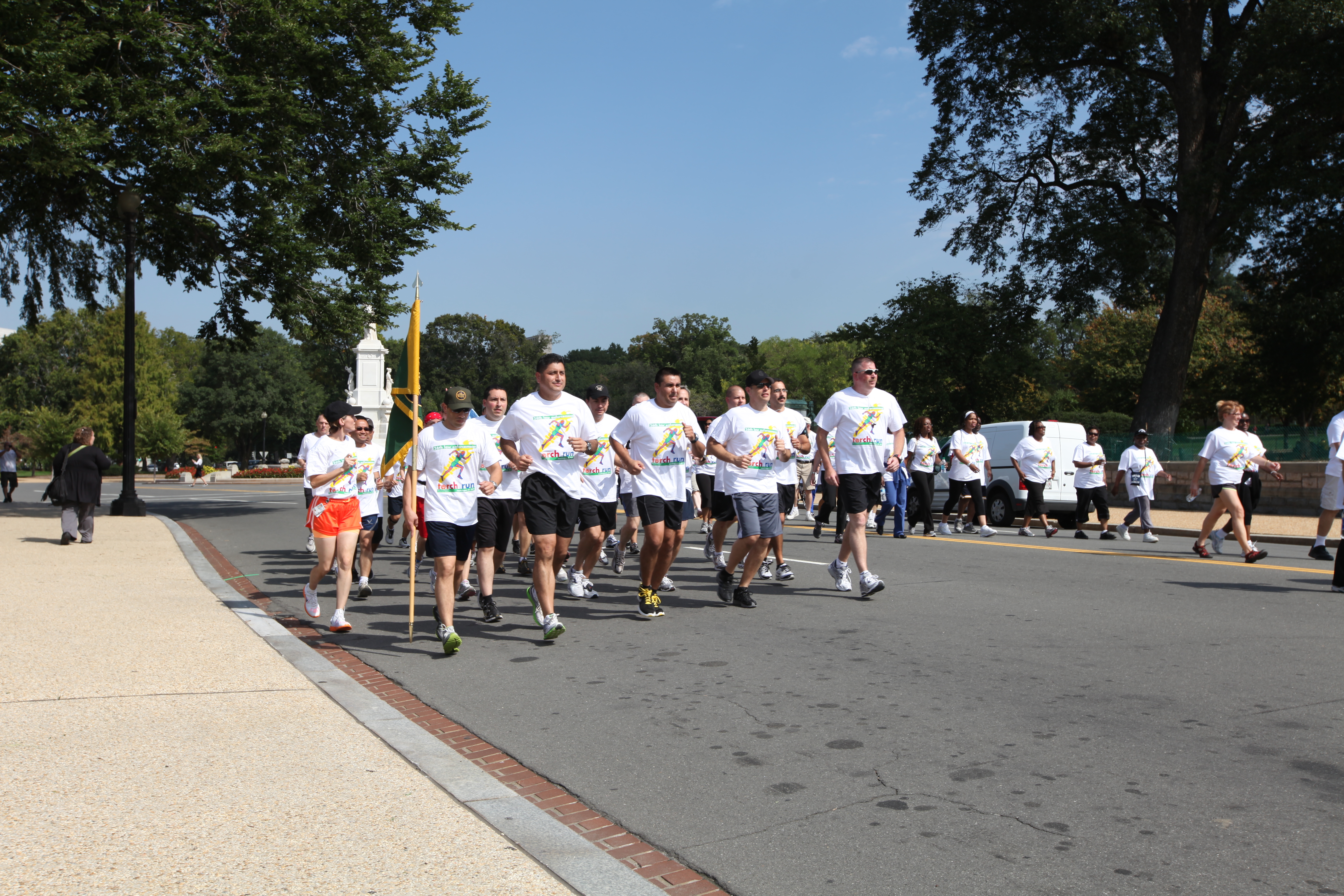 Dozens of runners in white shirts jog along a tree-lined road during a charity run.