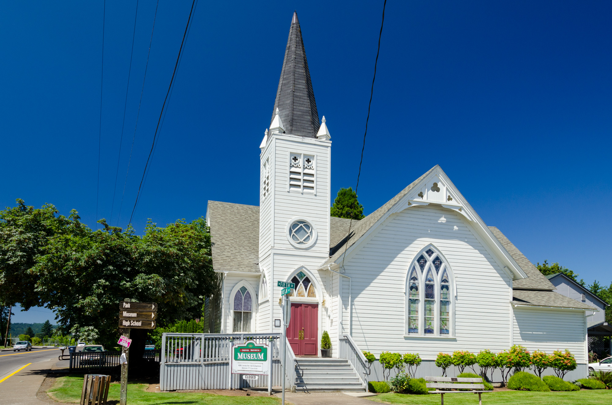 White church-style building with tall steeple and arched windows under blue sky.