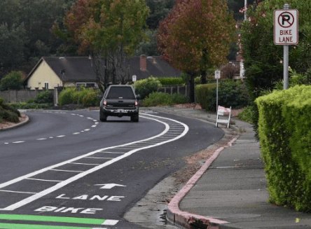 A curved road with a green painted bike lane and a no-parking sign, with a car driving away.
