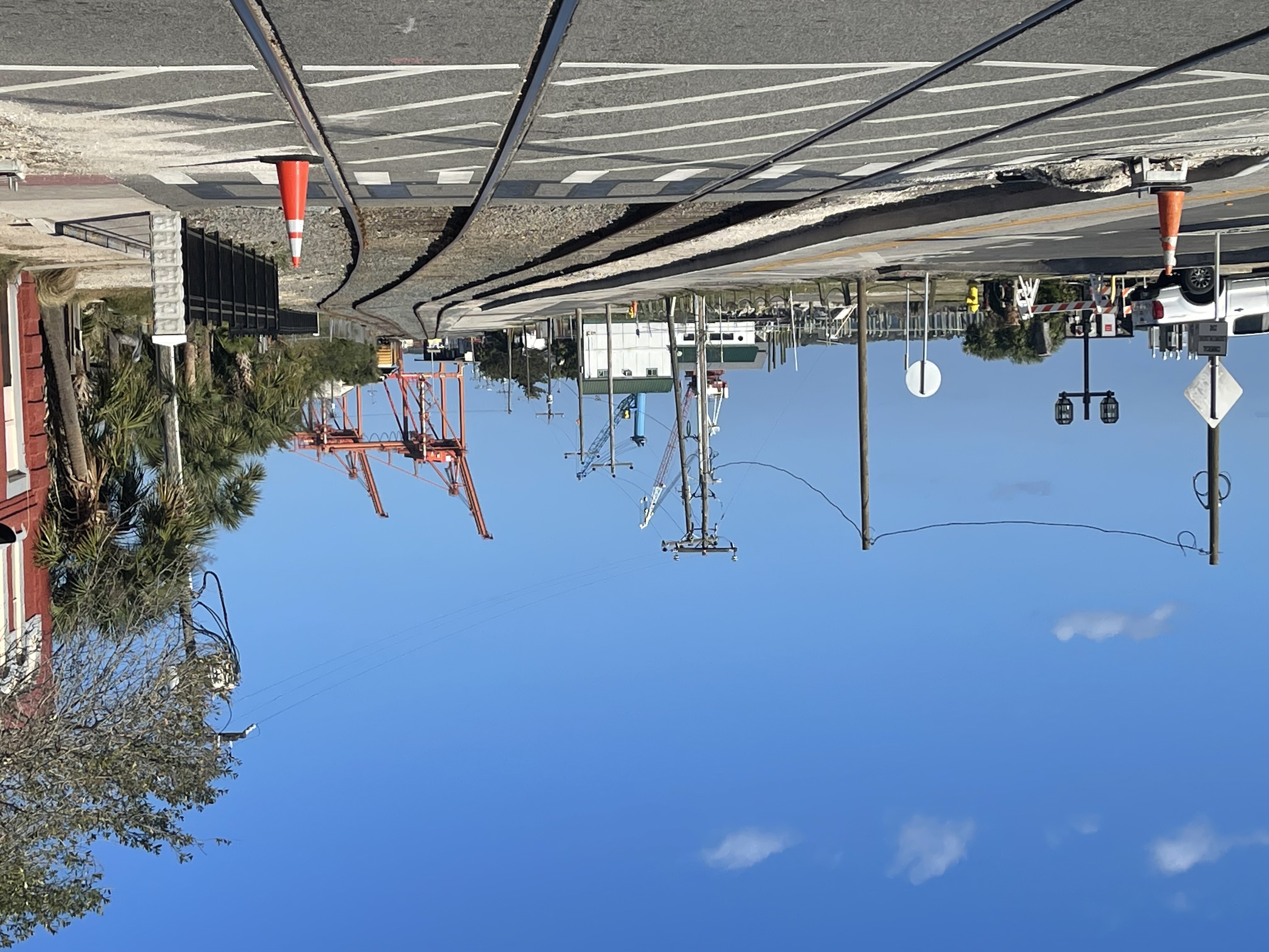 Railroad tracks run along a downtown street lined with palm trees and utility poles.