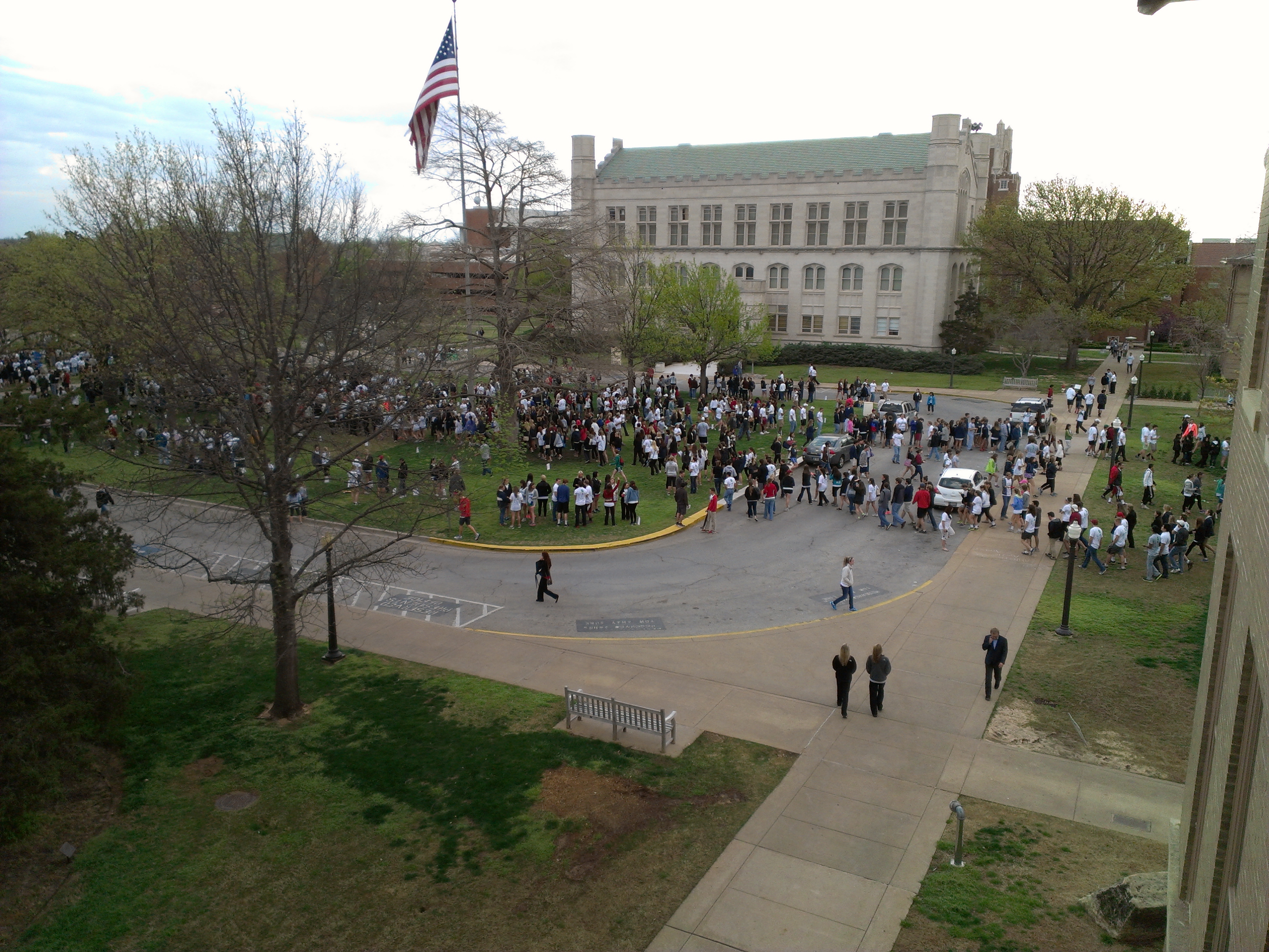 Large crowd of students on a university campus oval with a brick building behind them.