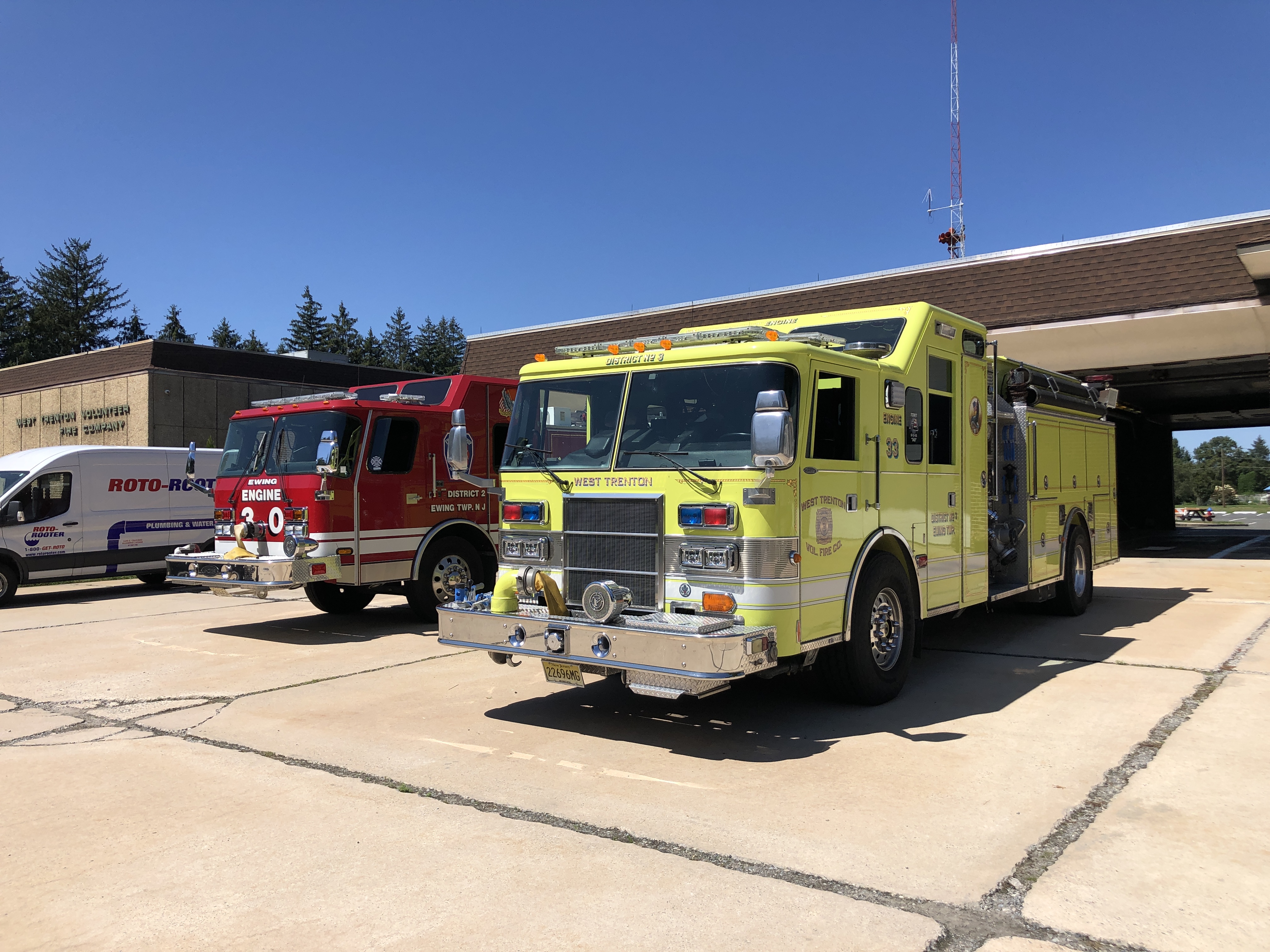 Two fire engines, one yellow-green and one red, parked outside a fire station on a clear day.