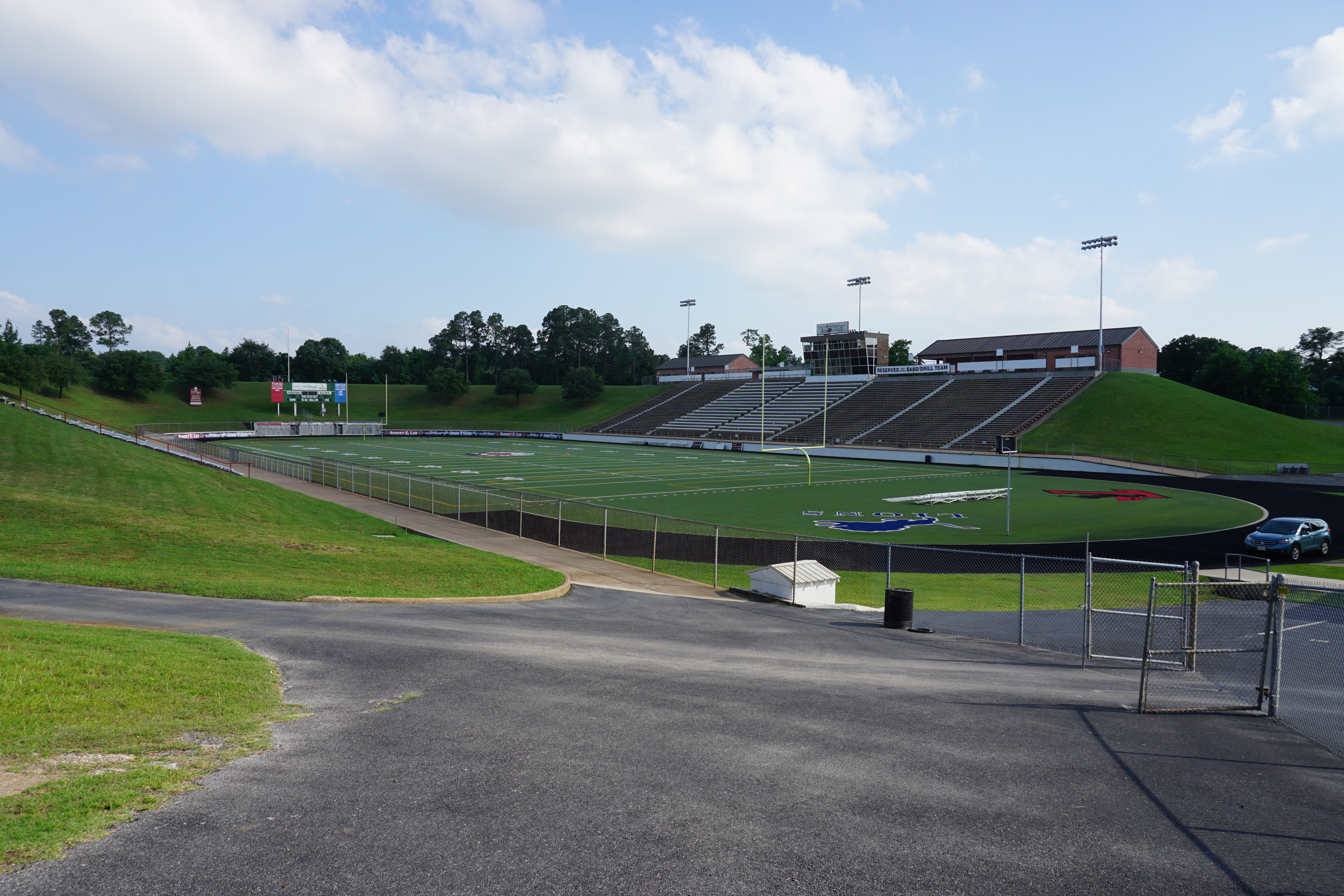 Outdoor football stadium with green turf, bleacher seating, and tall light poles.