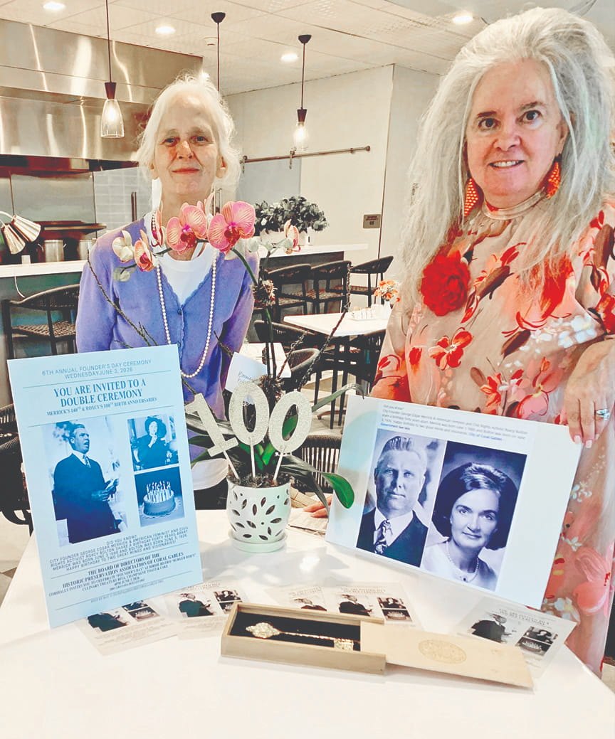 Two women standing behind a table with framed portraits, orchids, and a decorative 100 centerpiece at an indoor event.