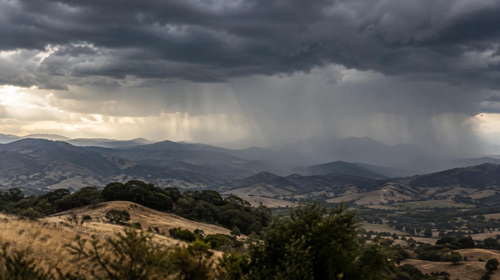 Dark storm clouds gather over rolling hills with rain visible in the distance.