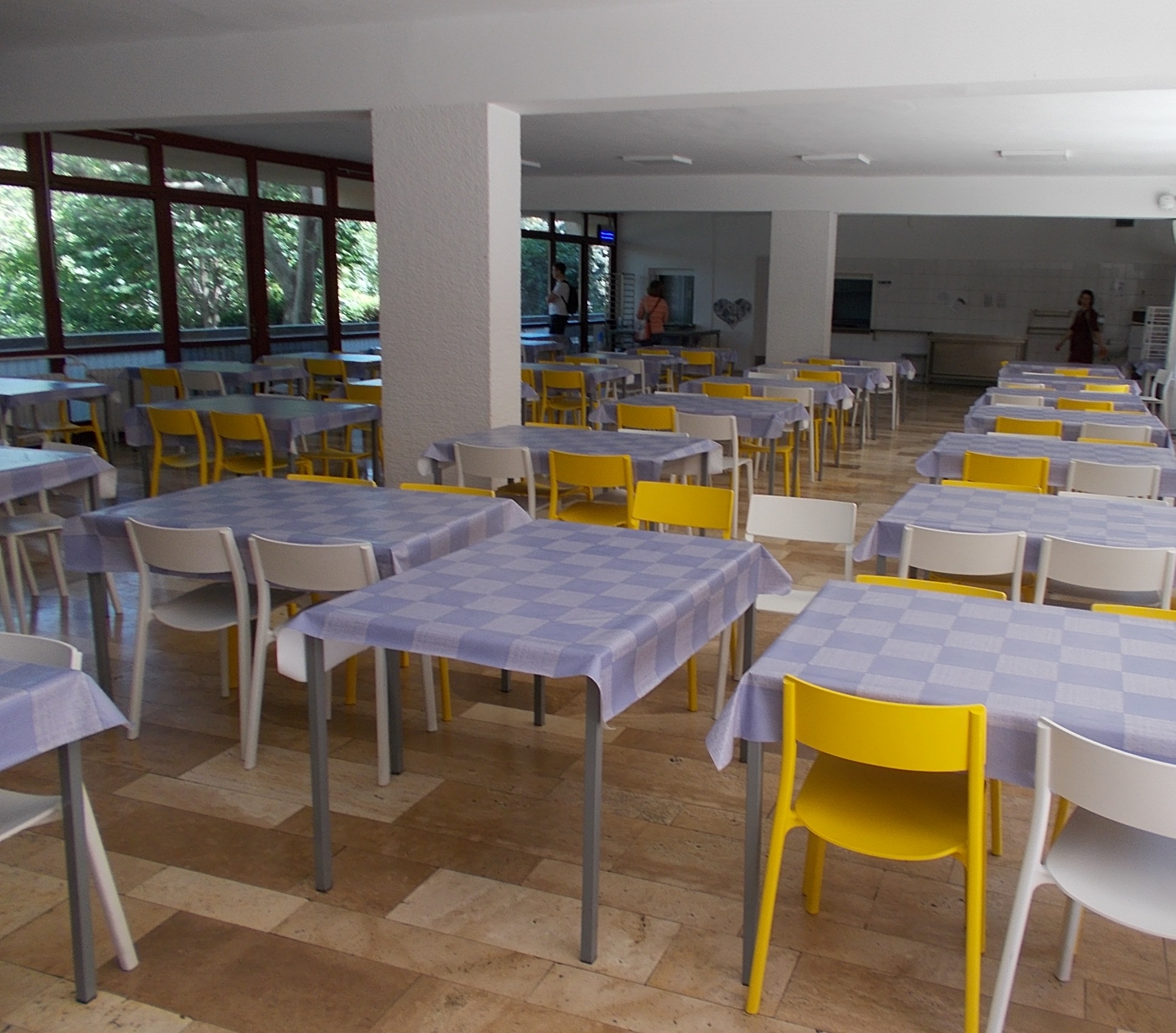 Empty school cafeteria with blue-checkered tablecloths and rows of plastic chairs.