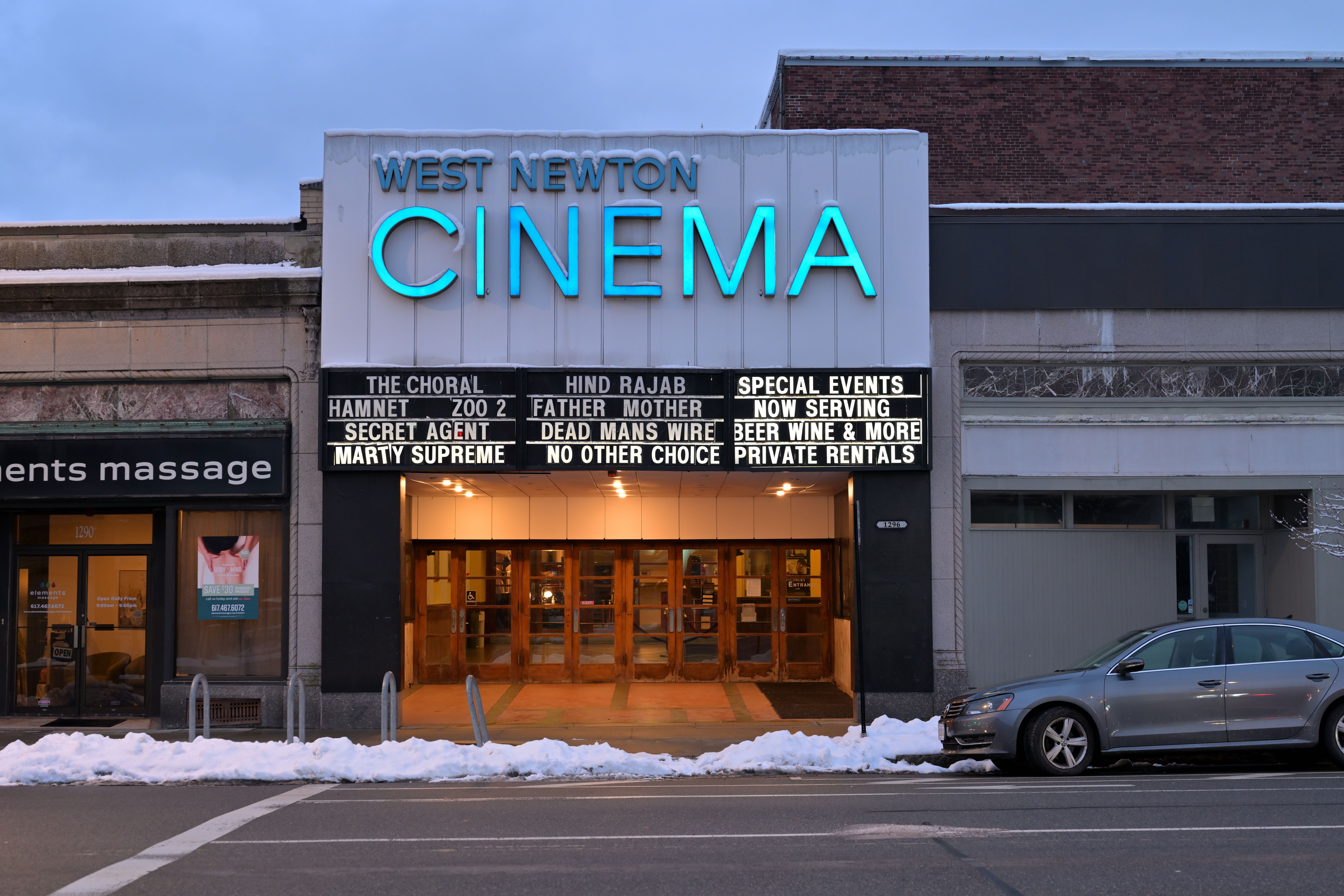 Illuminated marquee of West Newton Cinema at dusk, snow on the ground.