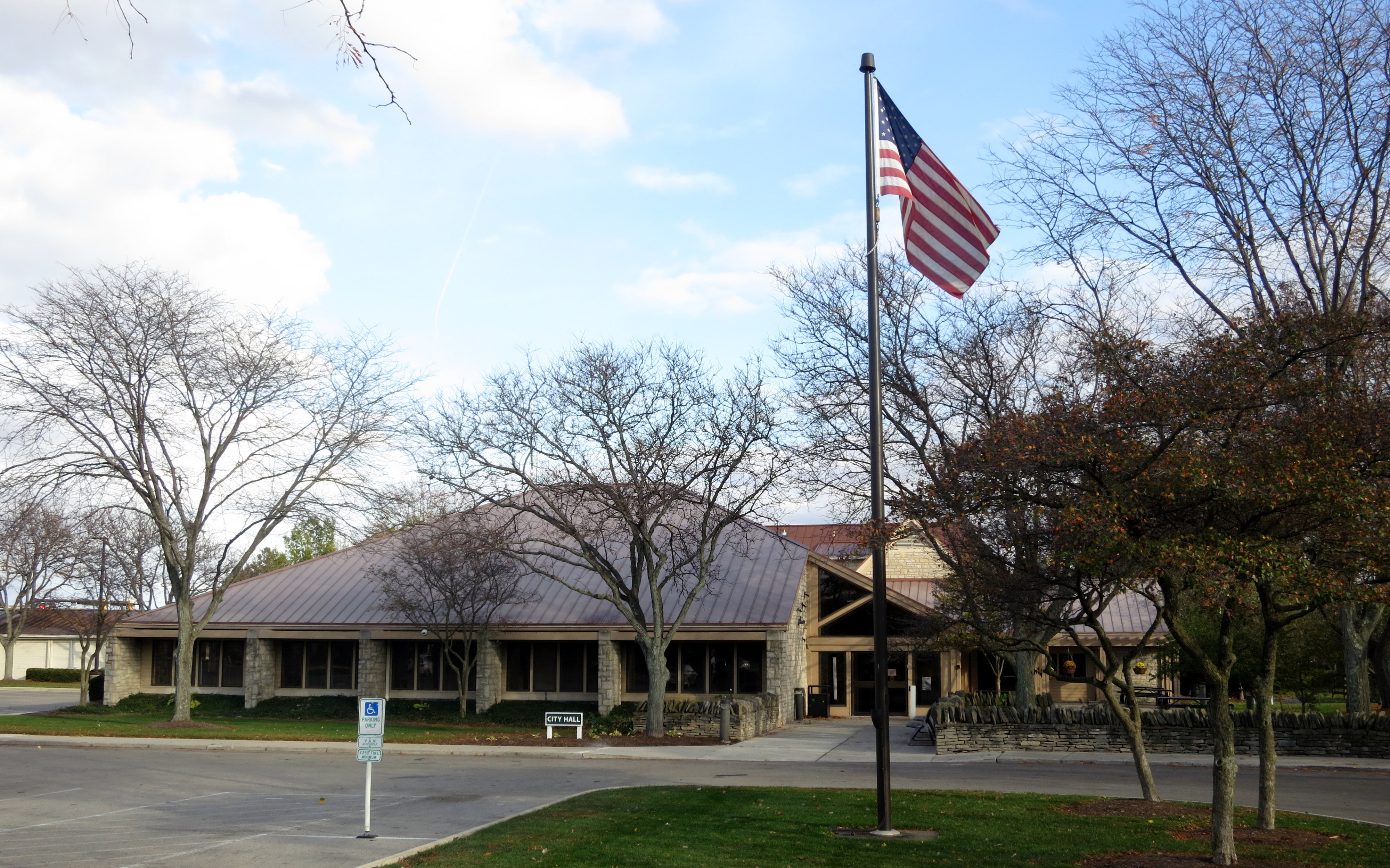 Low-rise stone building with metal roof and American flag on a flagpole, surrounded by bare trees.