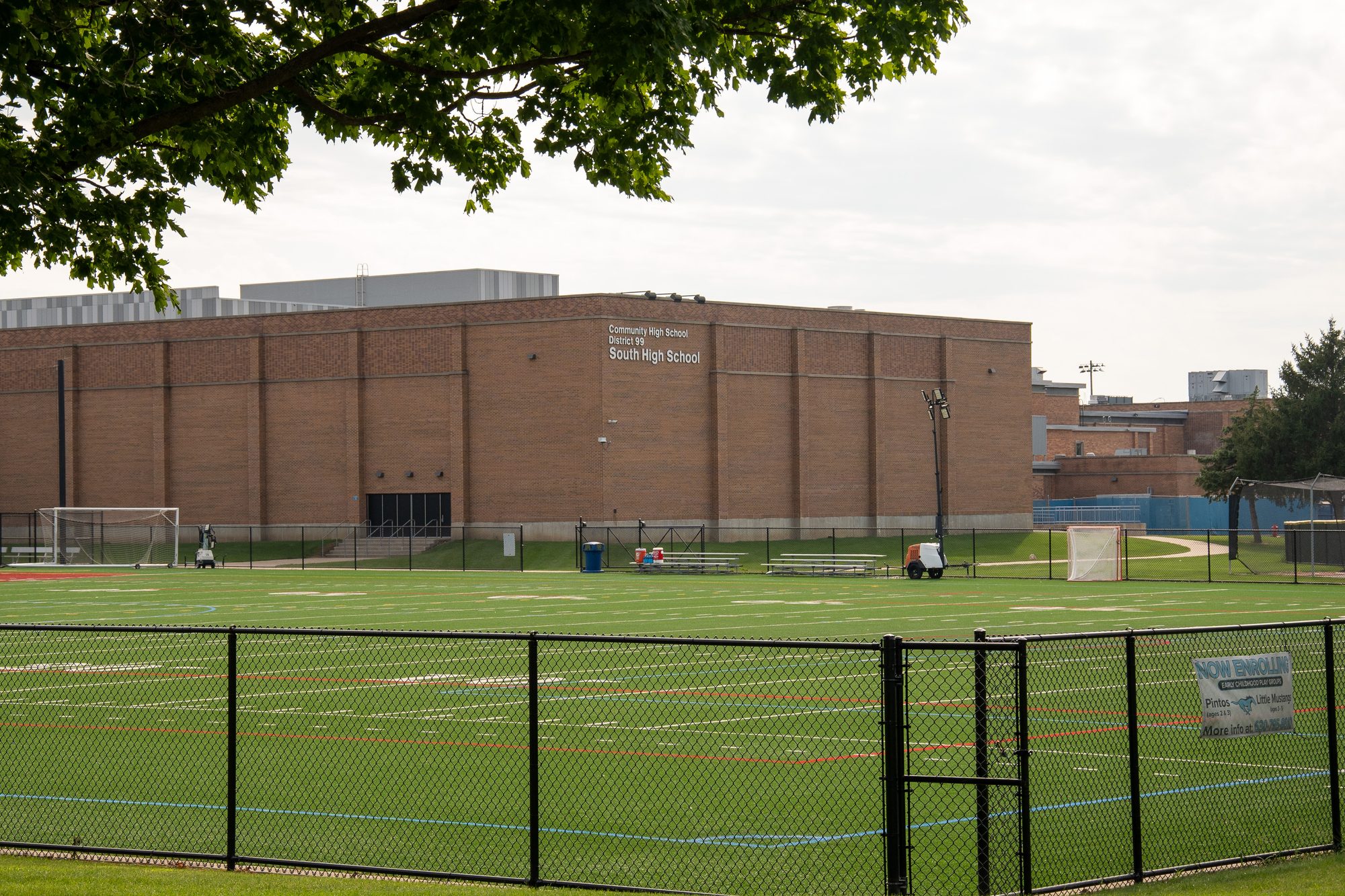 Brick high school building behind a fenced green artificial turf soccer field.