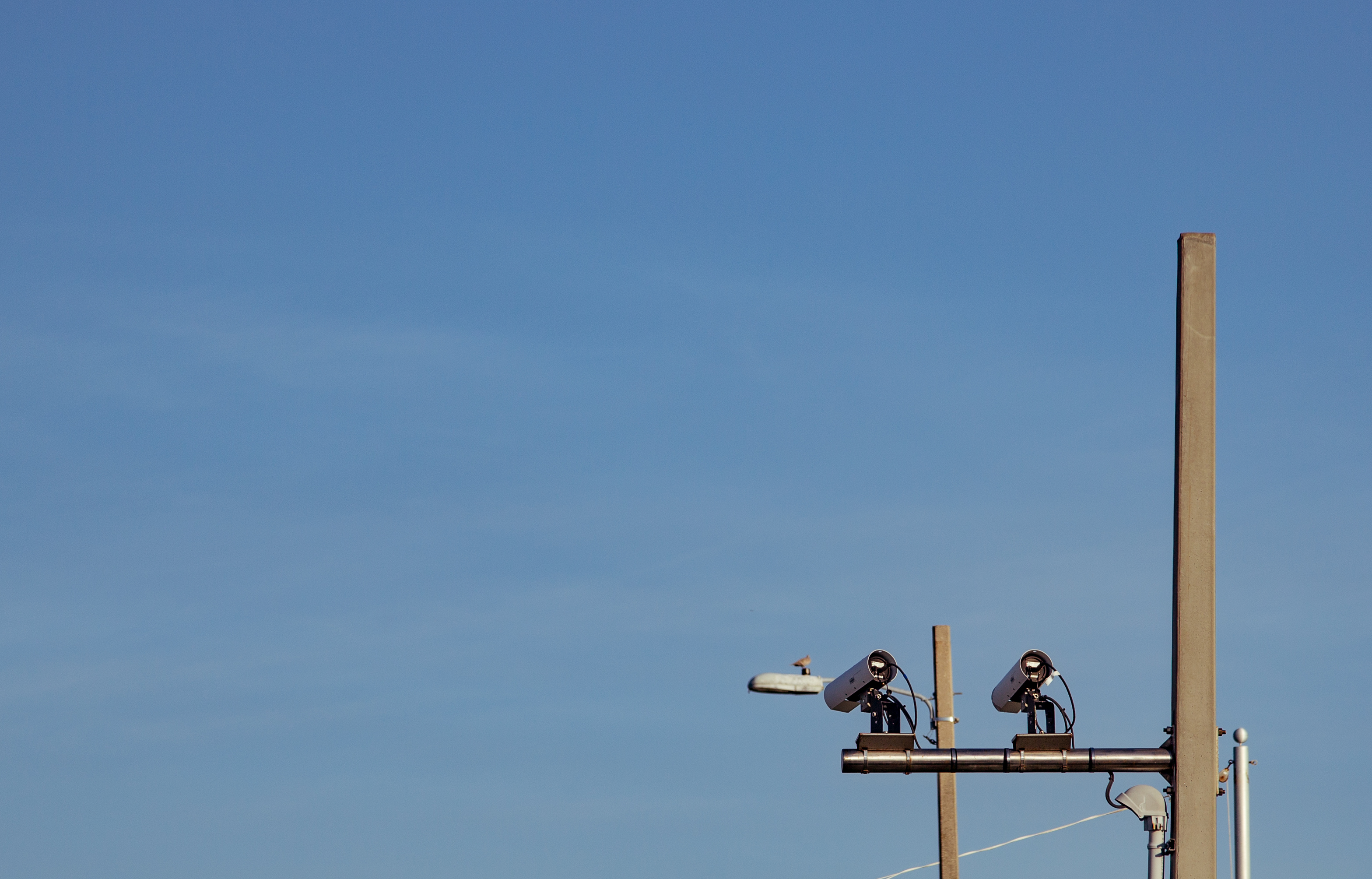 Two ALPR cameras and a street light mounted on a utility pole against a blue sky.