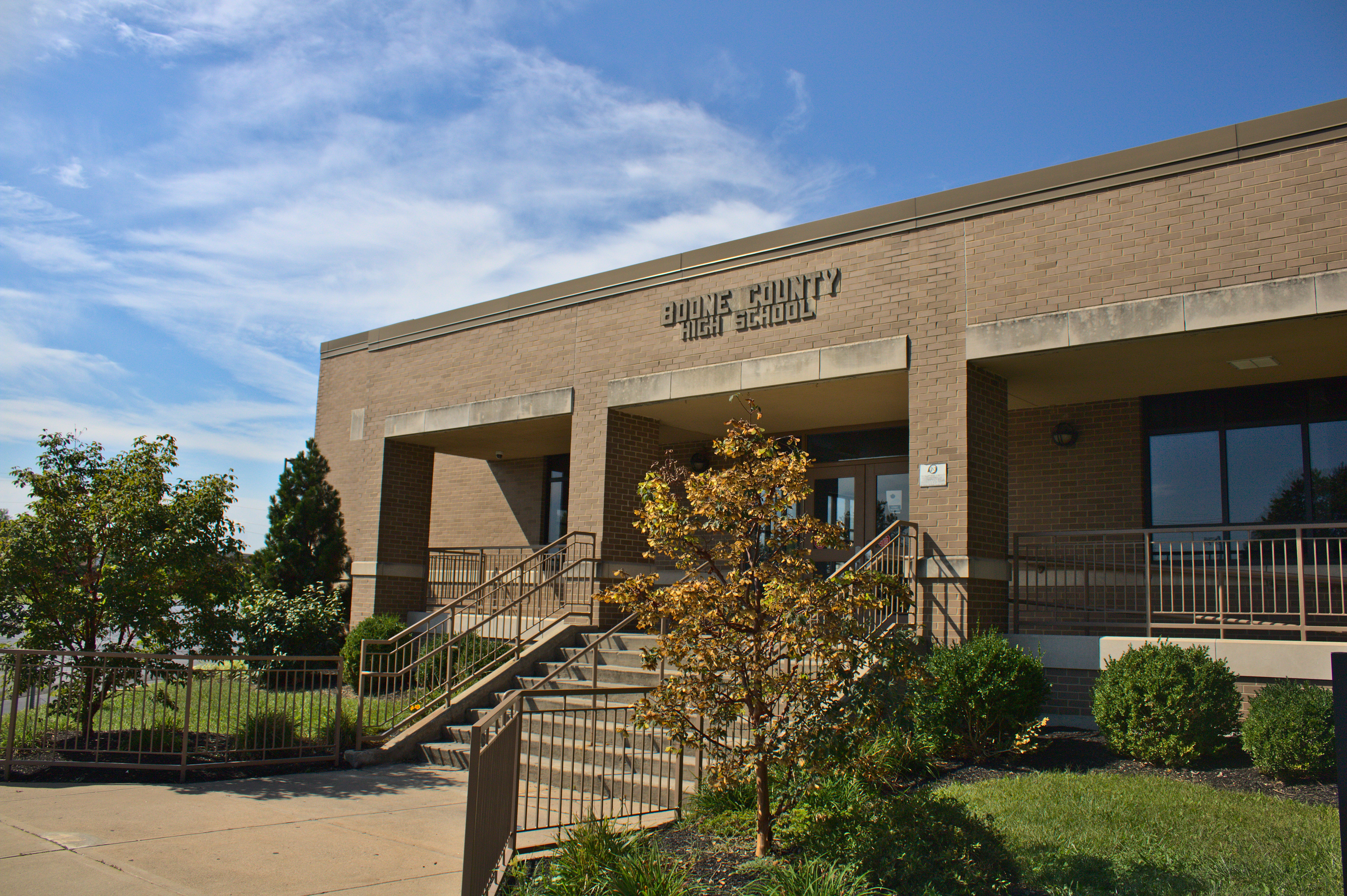 Exterior entrance of a tan brick high school building with metal railings and steps.
