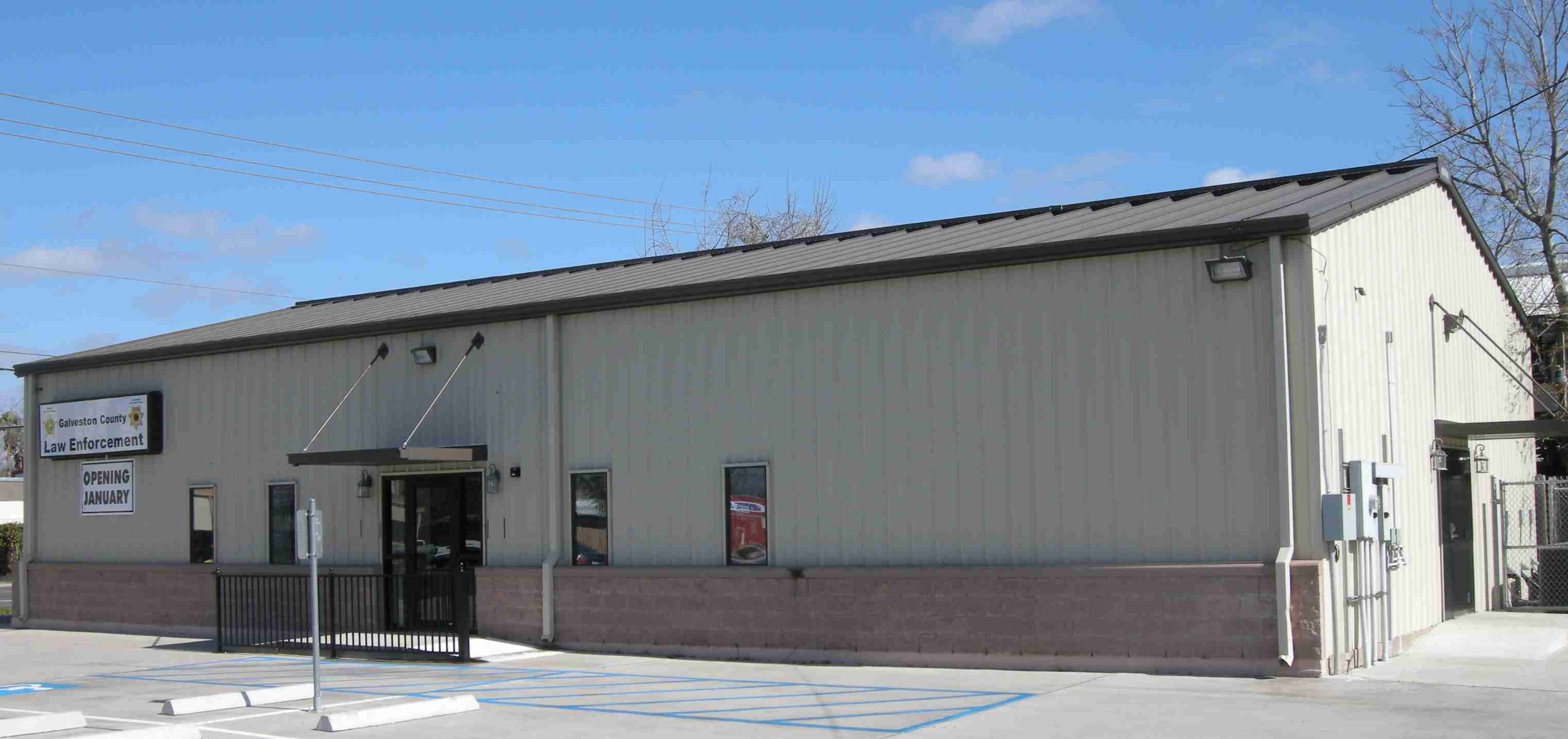 Single-story metal-sided law enforcement building with parking lot under blue sky.