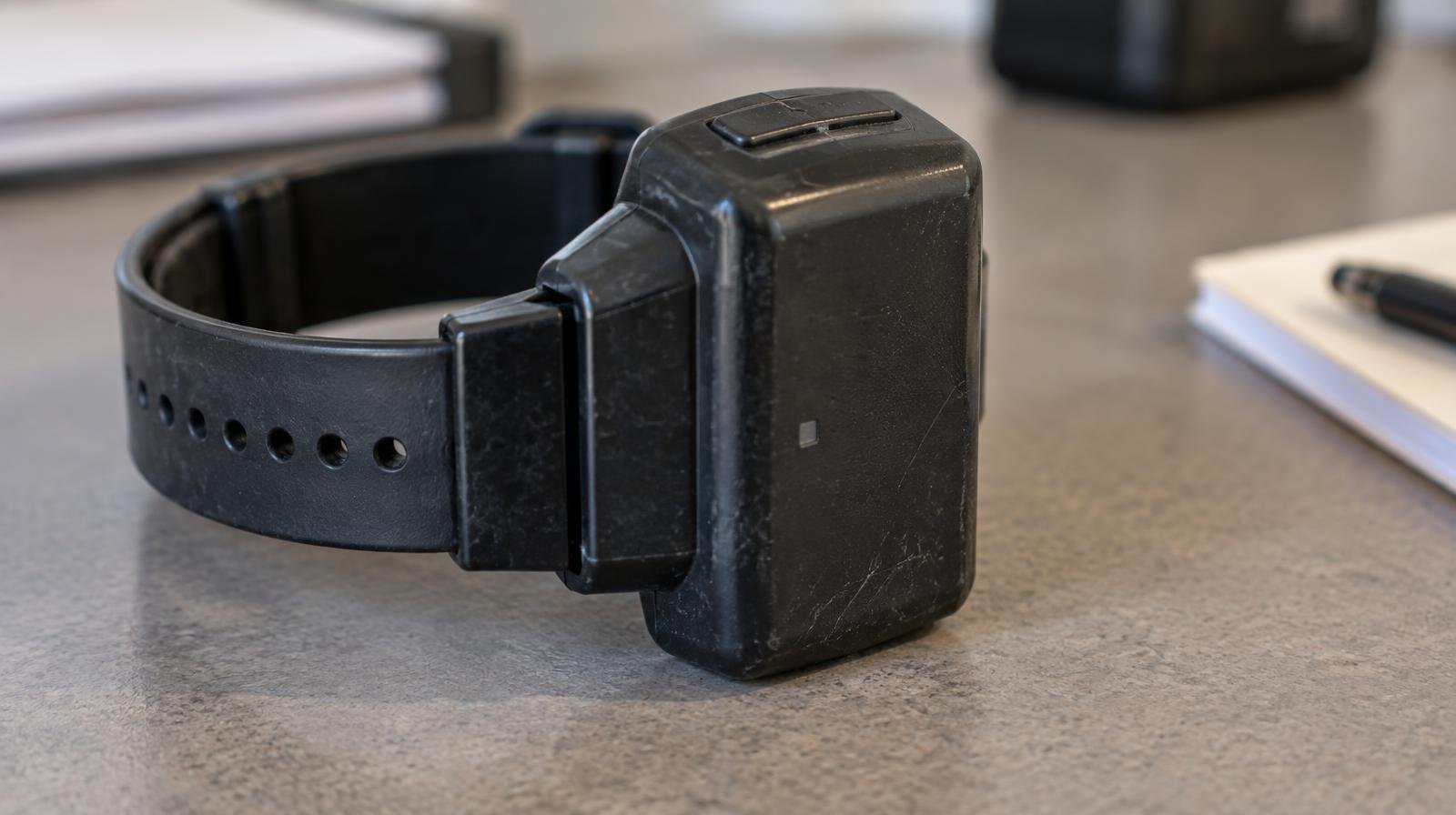 A GPS electronic ankle monitoring device with strap lying on a flat surface.