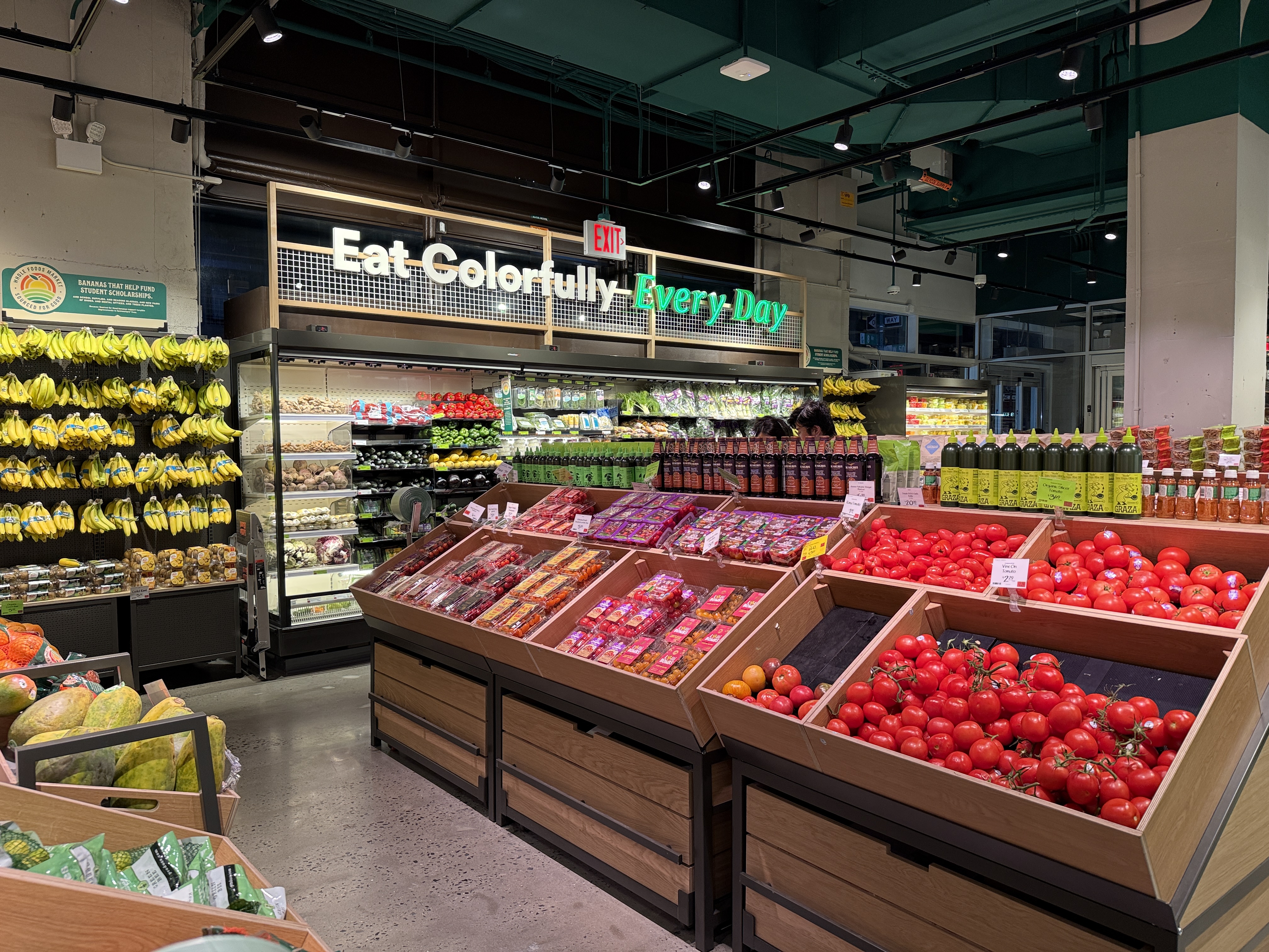 Colorful fresh produce displayed on wooden bins inside a Whole Foods Market store.