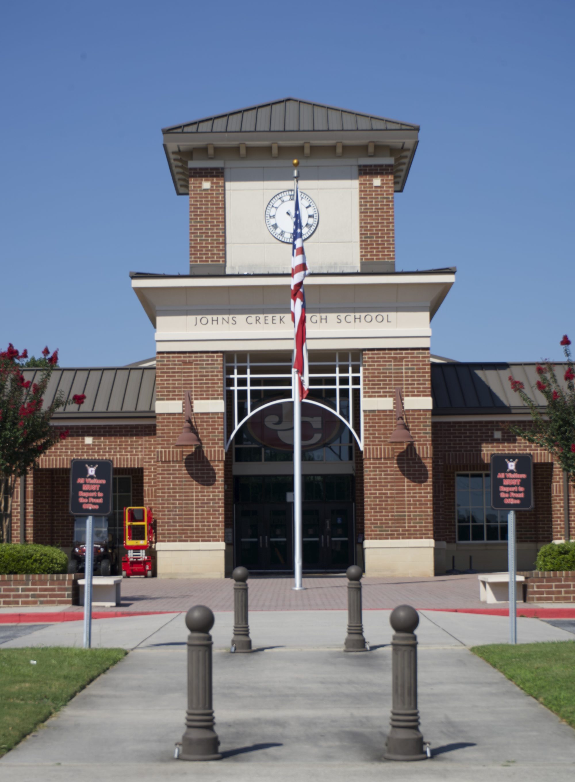 Brick high school building with central clock tower, arched entrance, and flagpole.