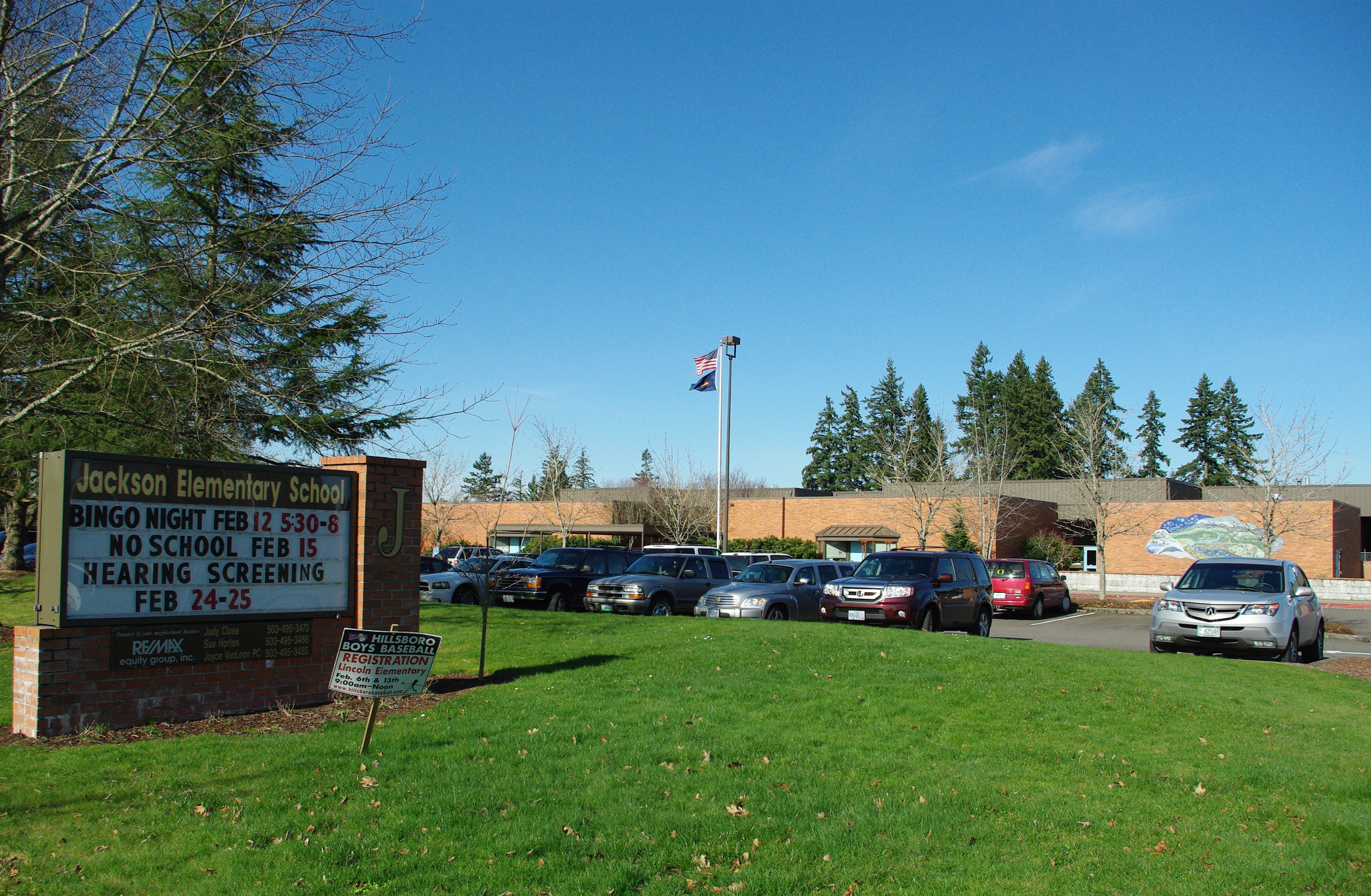 Exterior of a single-story brick elementary school with a marquee sign and flagpole.
