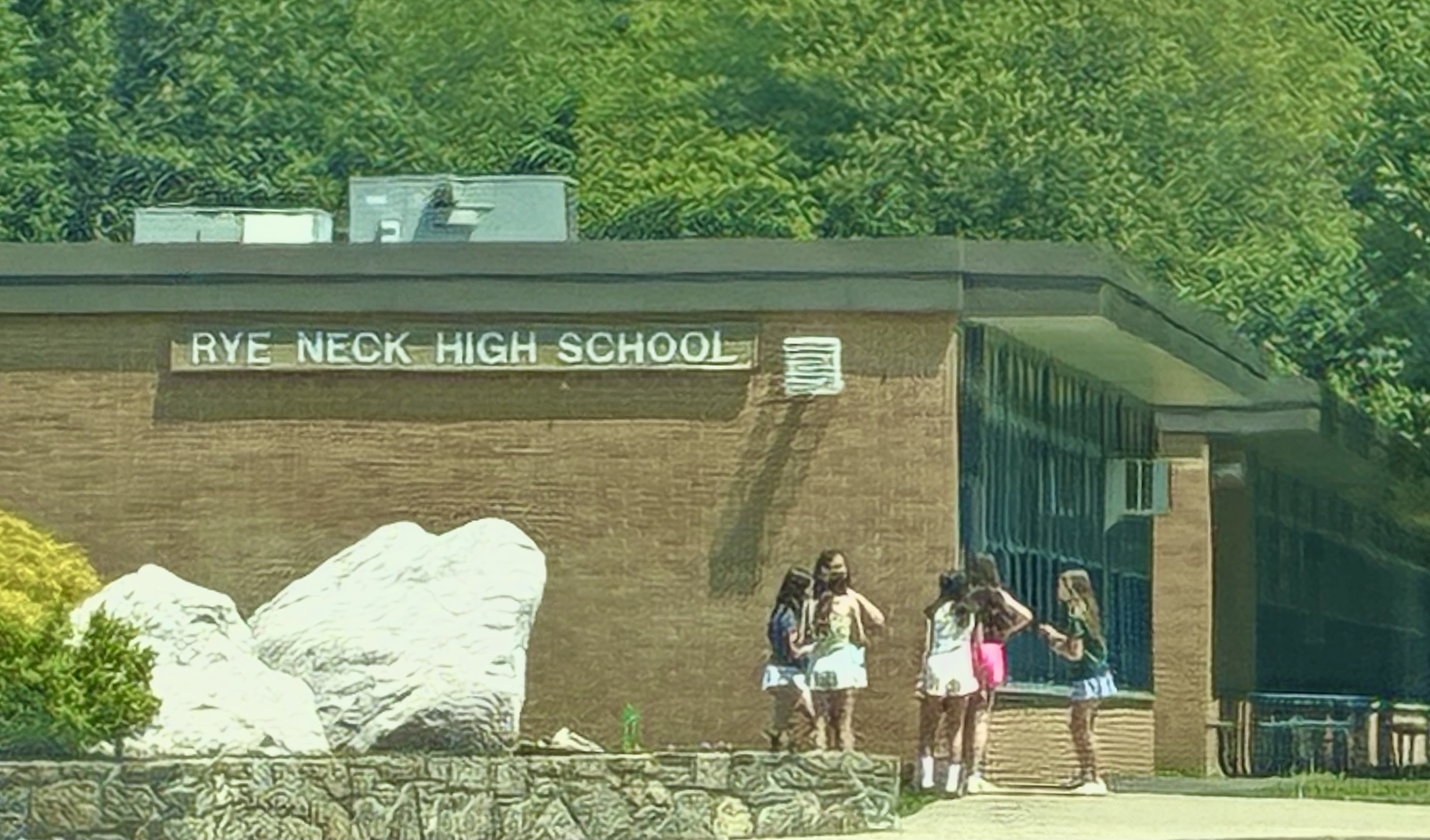 Brick school building with a sign reading Rye Neck High School and students near the entrance.