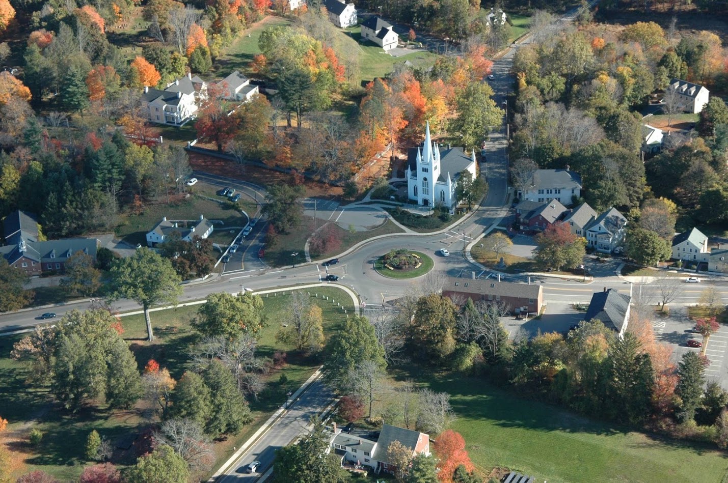 Aerial view of a New England town center with a white church steeple and autumn foliage.