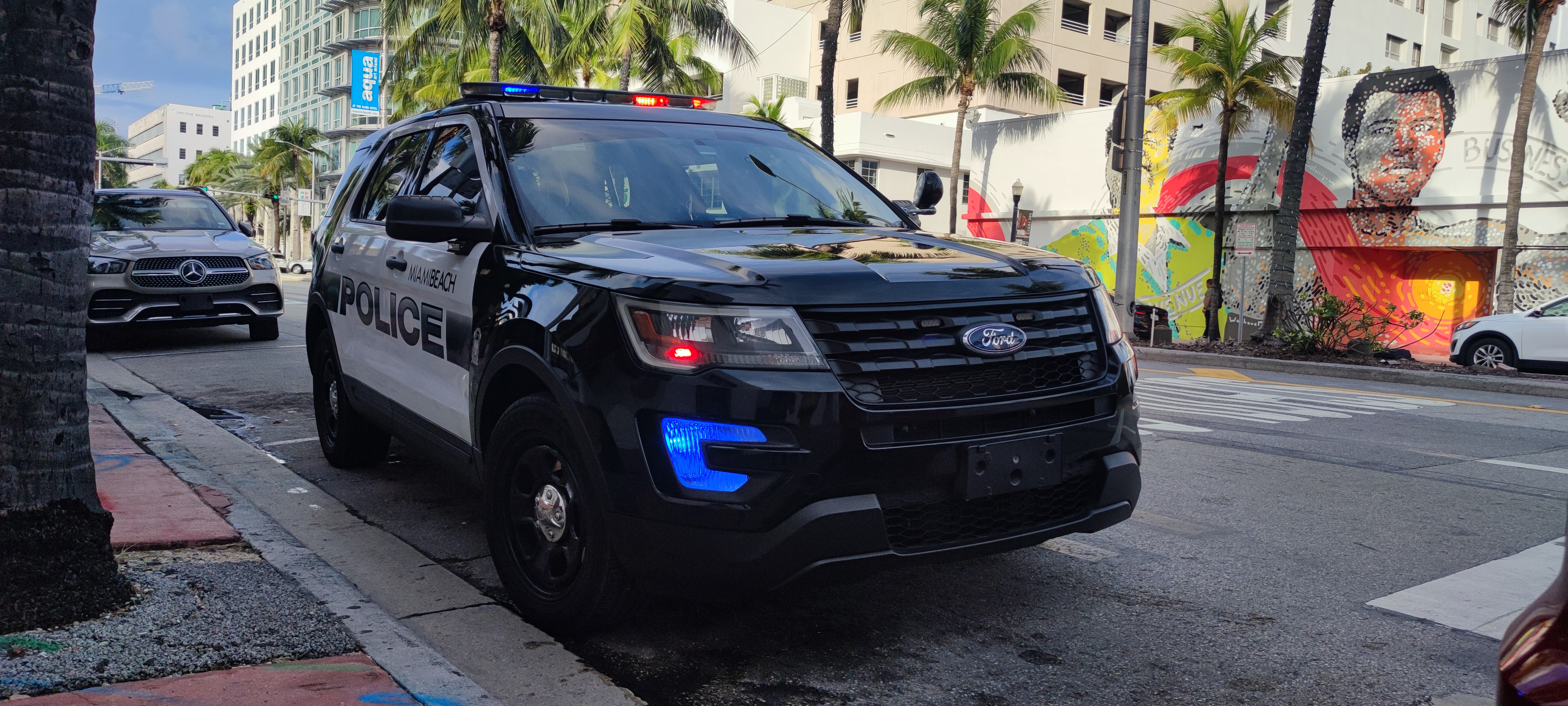 Miami Beach Police SUV with blue emergency lights on, parked on a city street.