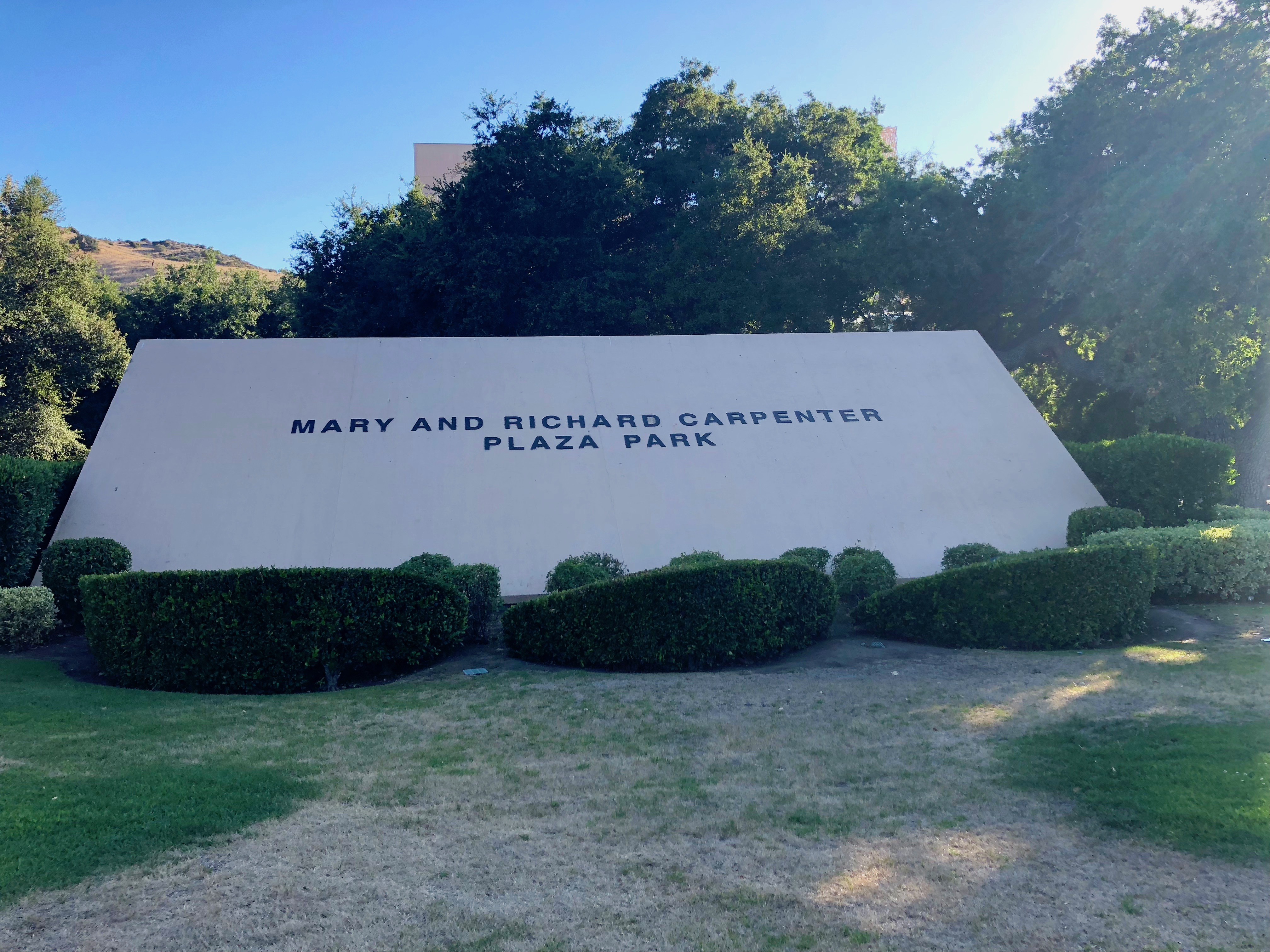 White monument sign at a civic campus surrounded by trimmed hedges and green lawn.