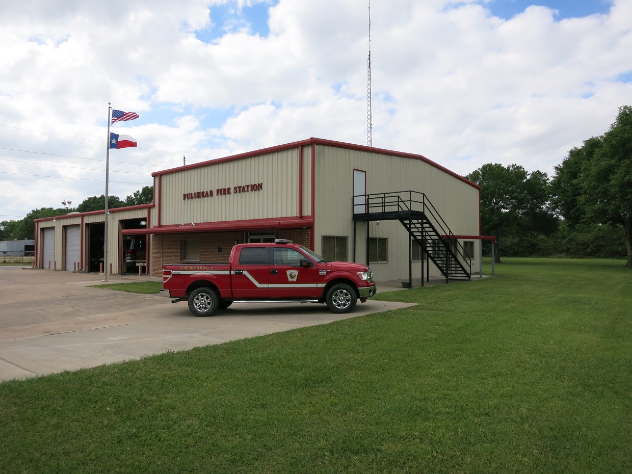 Metal fire station building with bay doors, flags, and a red fire department truck parked outside.