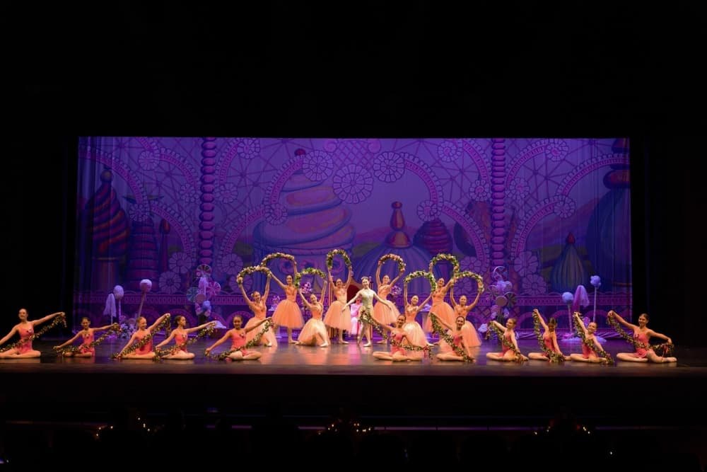 Ballet dancers in pink costumes perform on a colorful candy-themed stage set.
