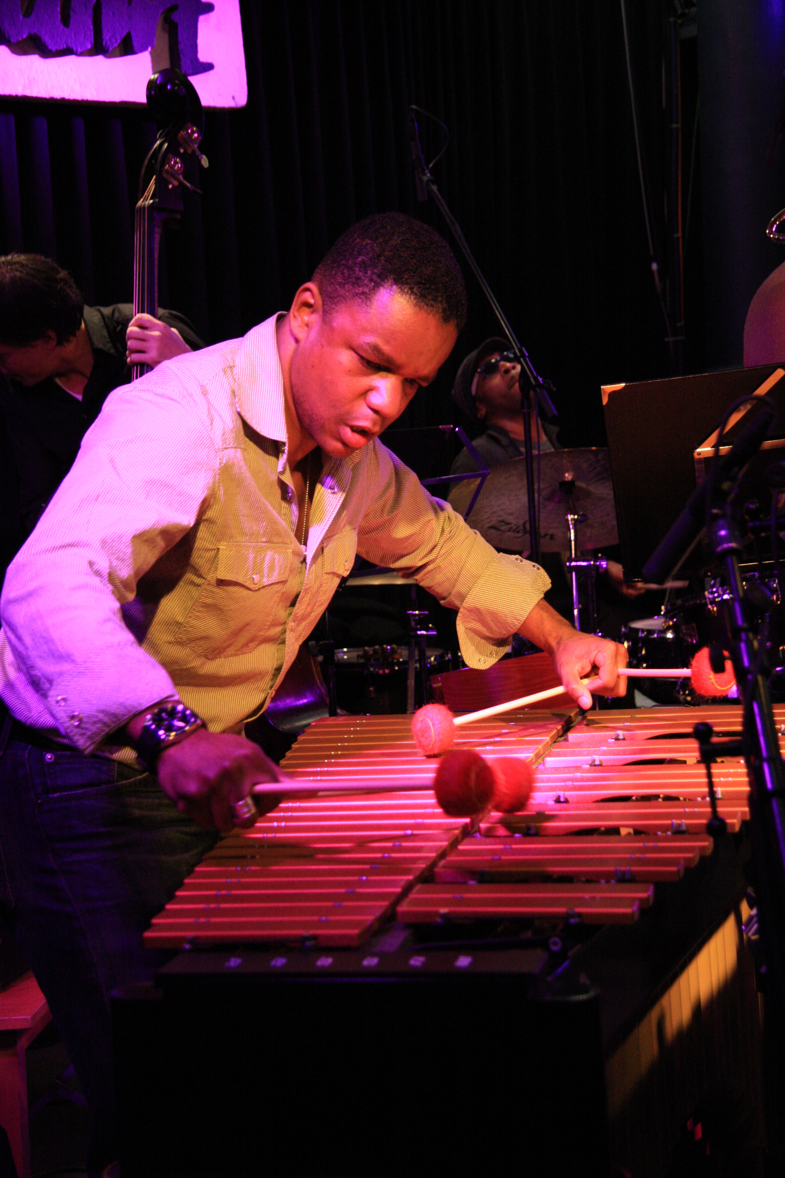 A musician leans over a vibraphone, striking the keys with mallets on stage.