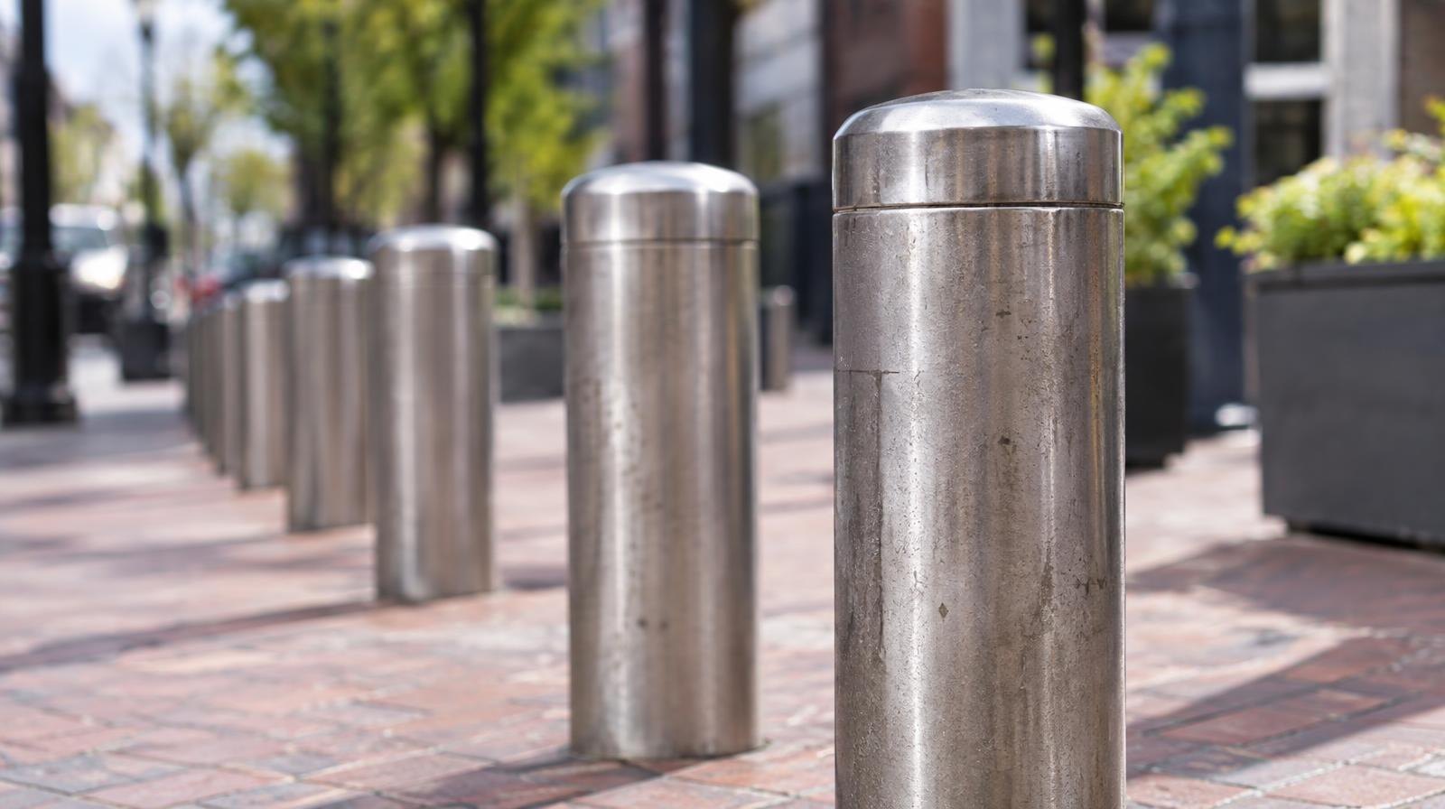 A row of metal bollards along a brick pedestrian plaza outdoors.