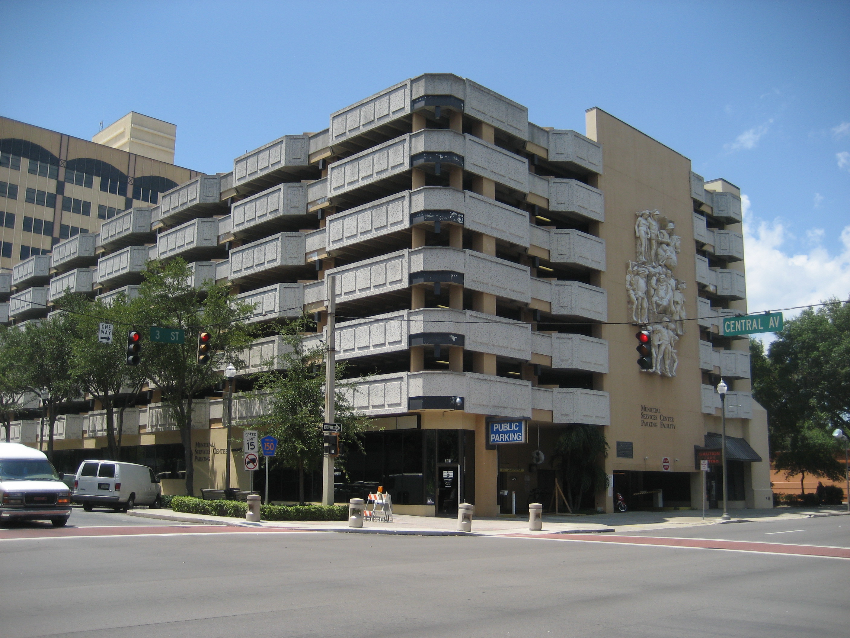 Multi-story open-air parking garage on a street corner with a Public Parking sign.
