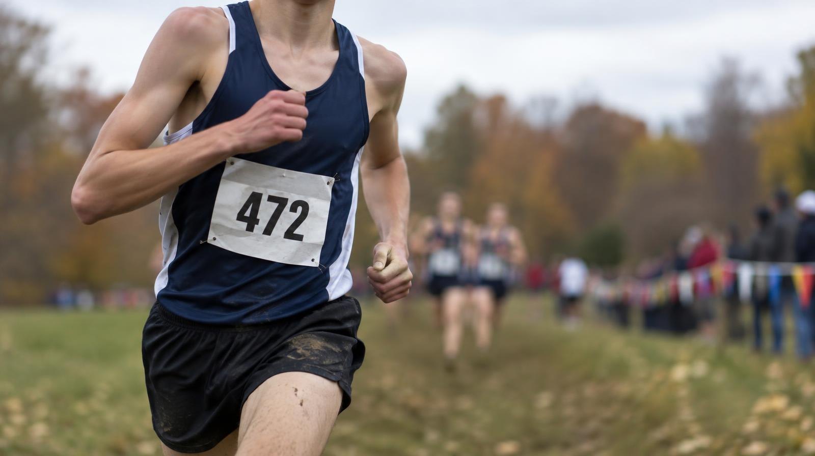 A male runner in mid-stride on a grass cross country course on an overcast autumn day.