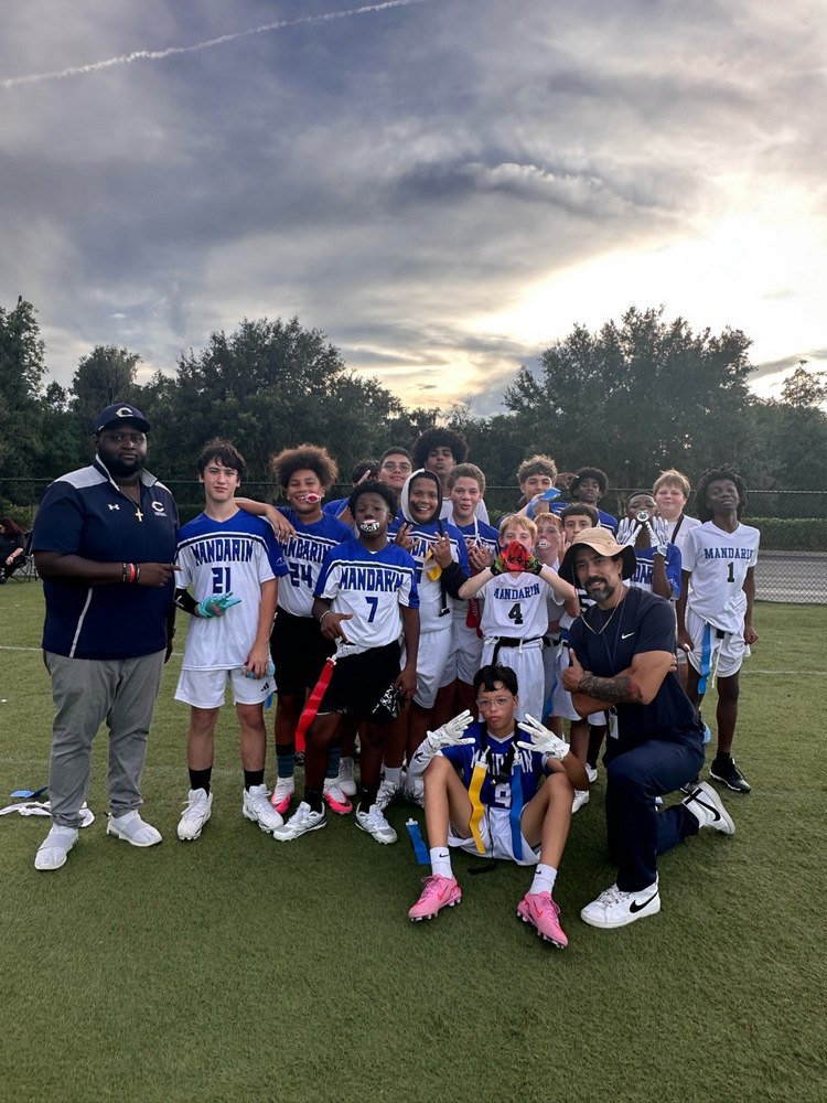 Youth flag football players in white and blue Mandarin jerseys pose with coaches on a field at dusk.