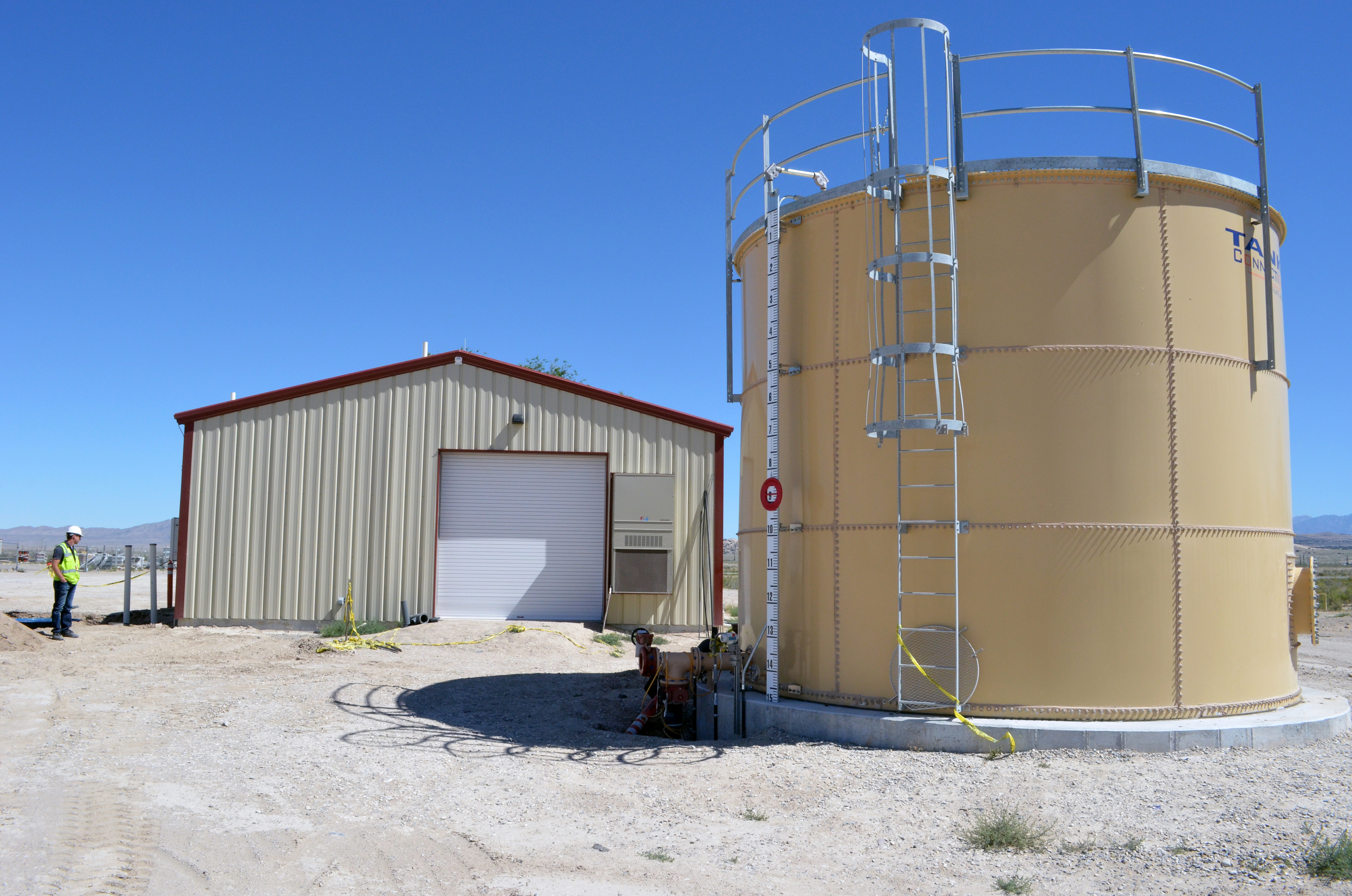 Large cylindrical water storage tank beside a metal utility building at a treatment facility.