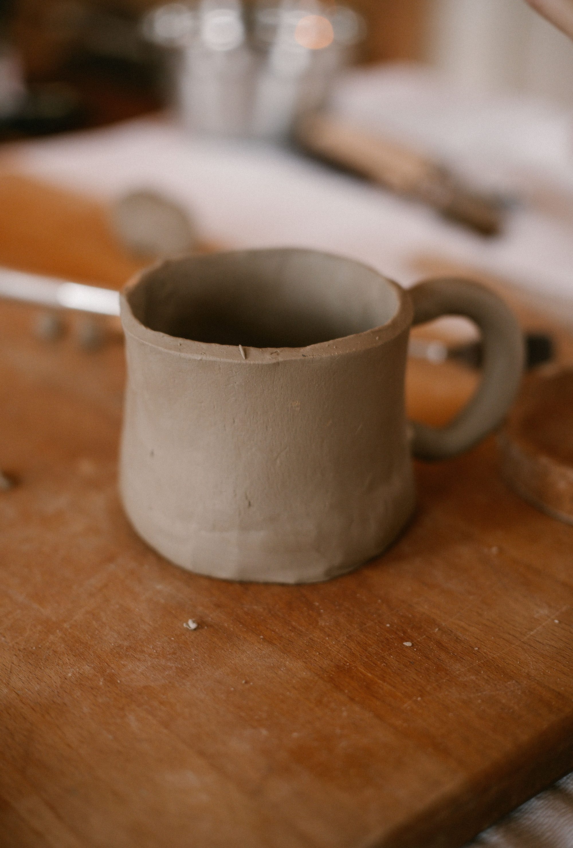 Rustic handmade clay mug placed on a wooden table in a pottery studio setting.