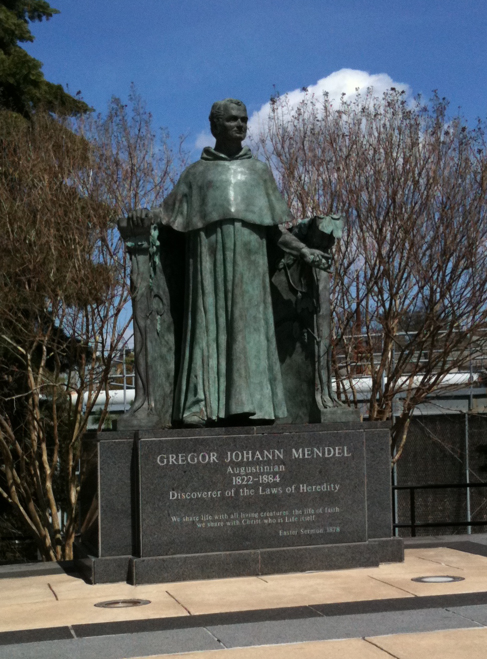 Bronze statue of a robed figure on a granite pedestal on a university campus.