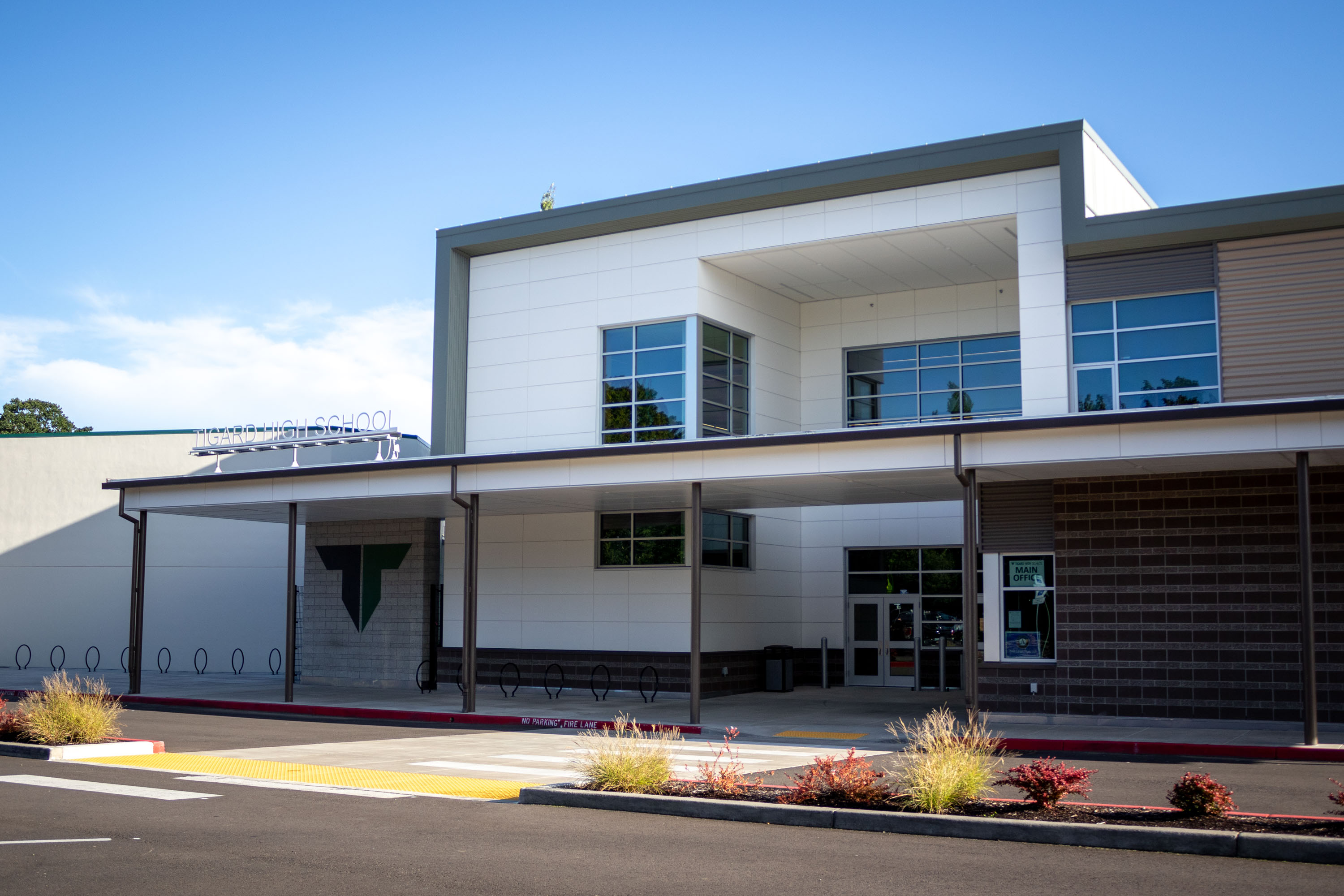 Modern two-story school building exterior with covered entrance and green logo on facade.