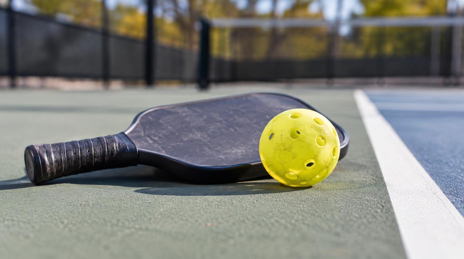 A yellow pickleball and paddle resting on an outdoor hard court.