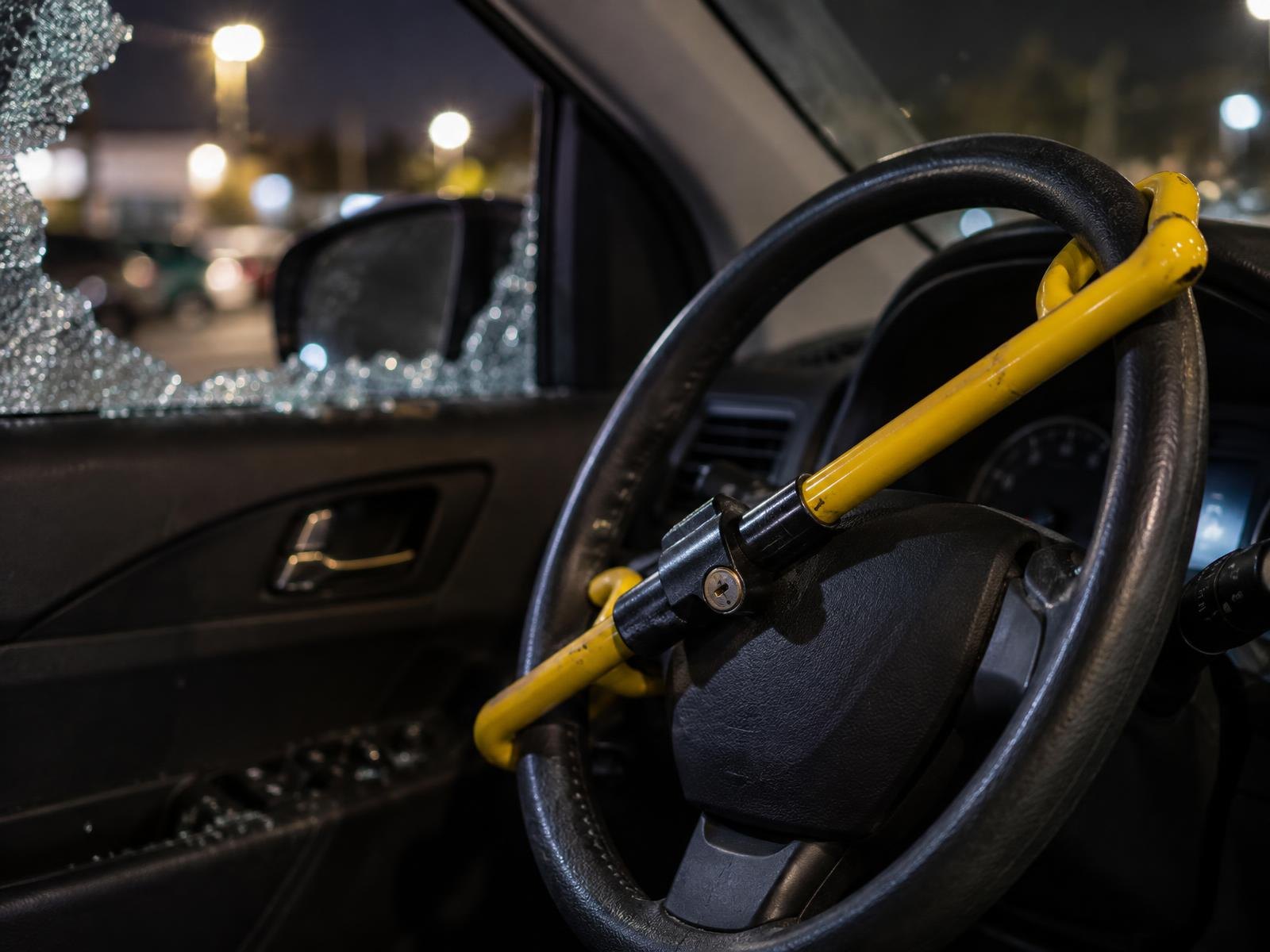 Yellow steering wheel club lock clamped on a steering wheel, broken car window behind it.