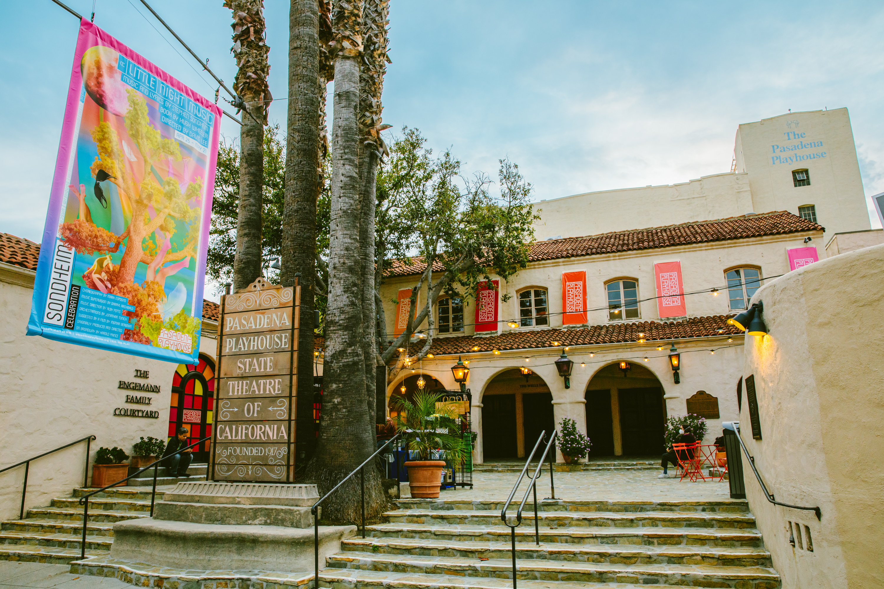 Exterior of a Spanish Colonial Revival theater with palm trees and red banners on the facade.