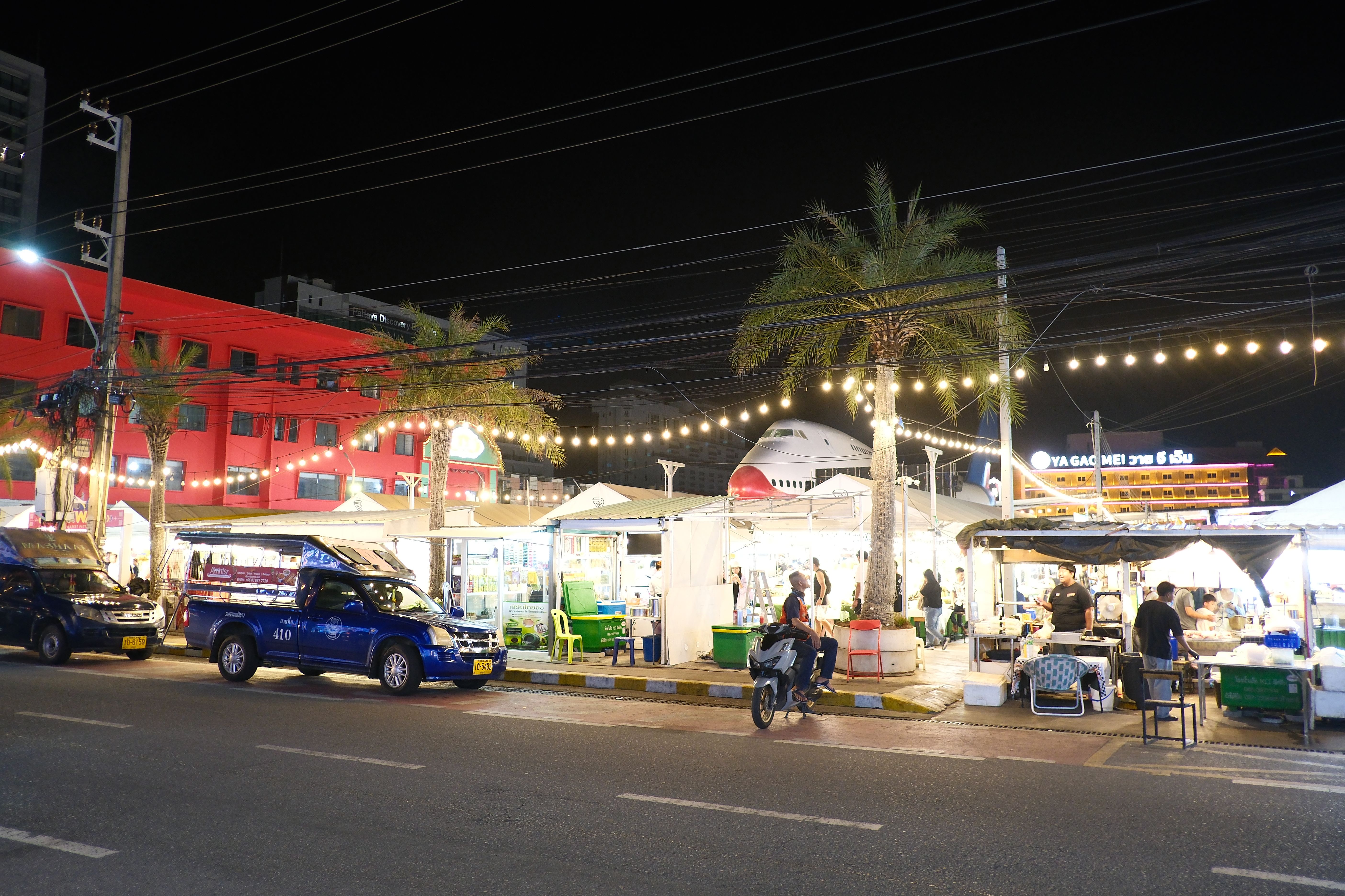 Outdoor night market with string lights, vendor stalls, and palm trees at night.