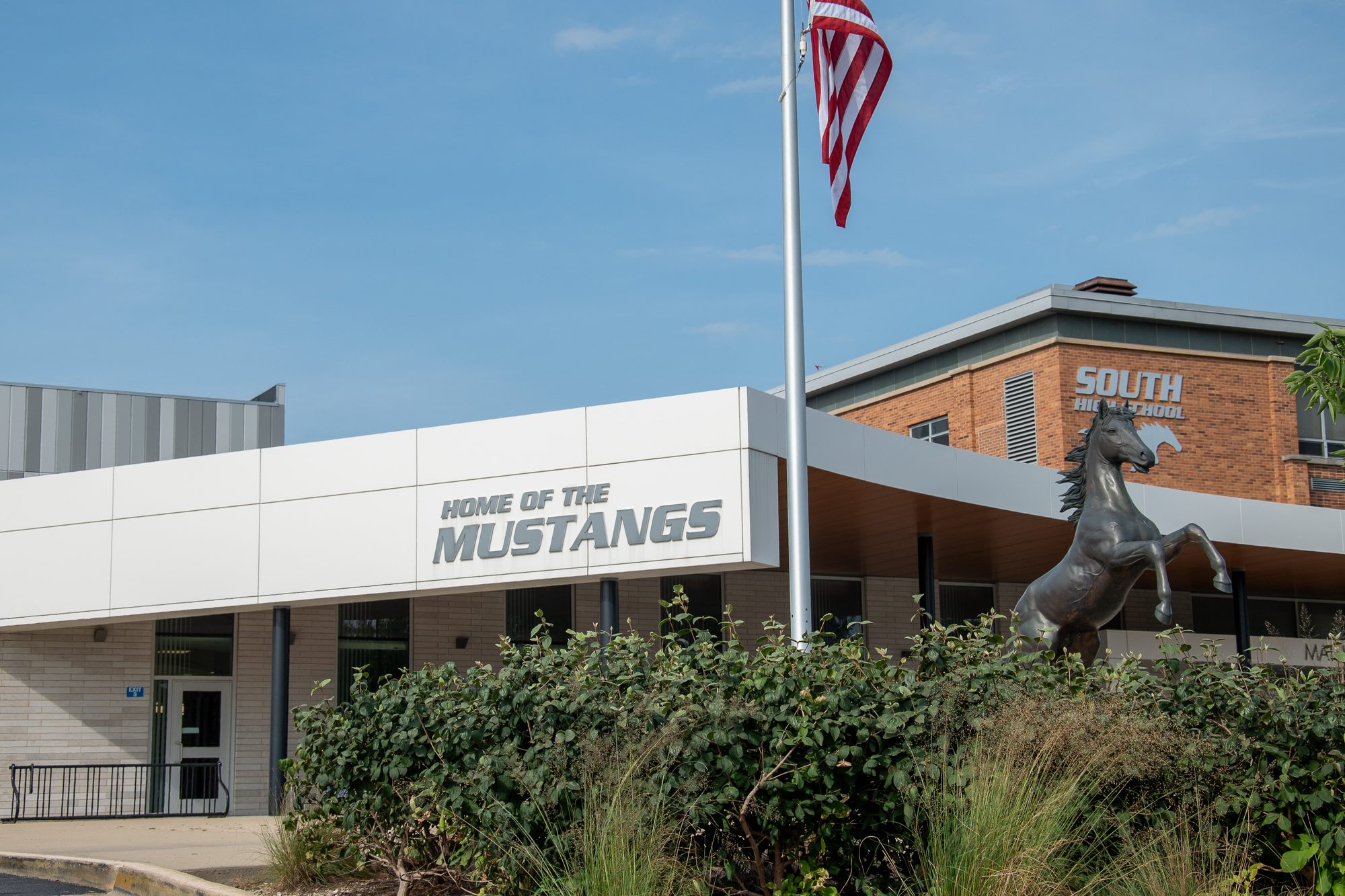 Exterior of a high school building with a rearing horse mascot statue and flagpole.