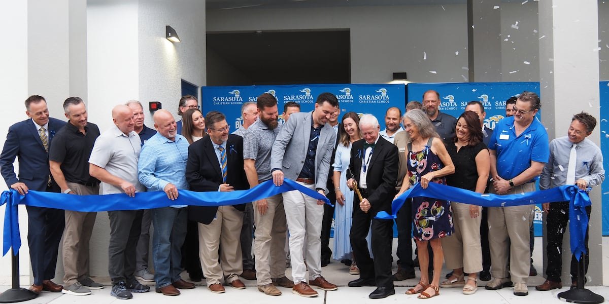 A group of people cutting a blue ribbon at a building entrance ceremony.