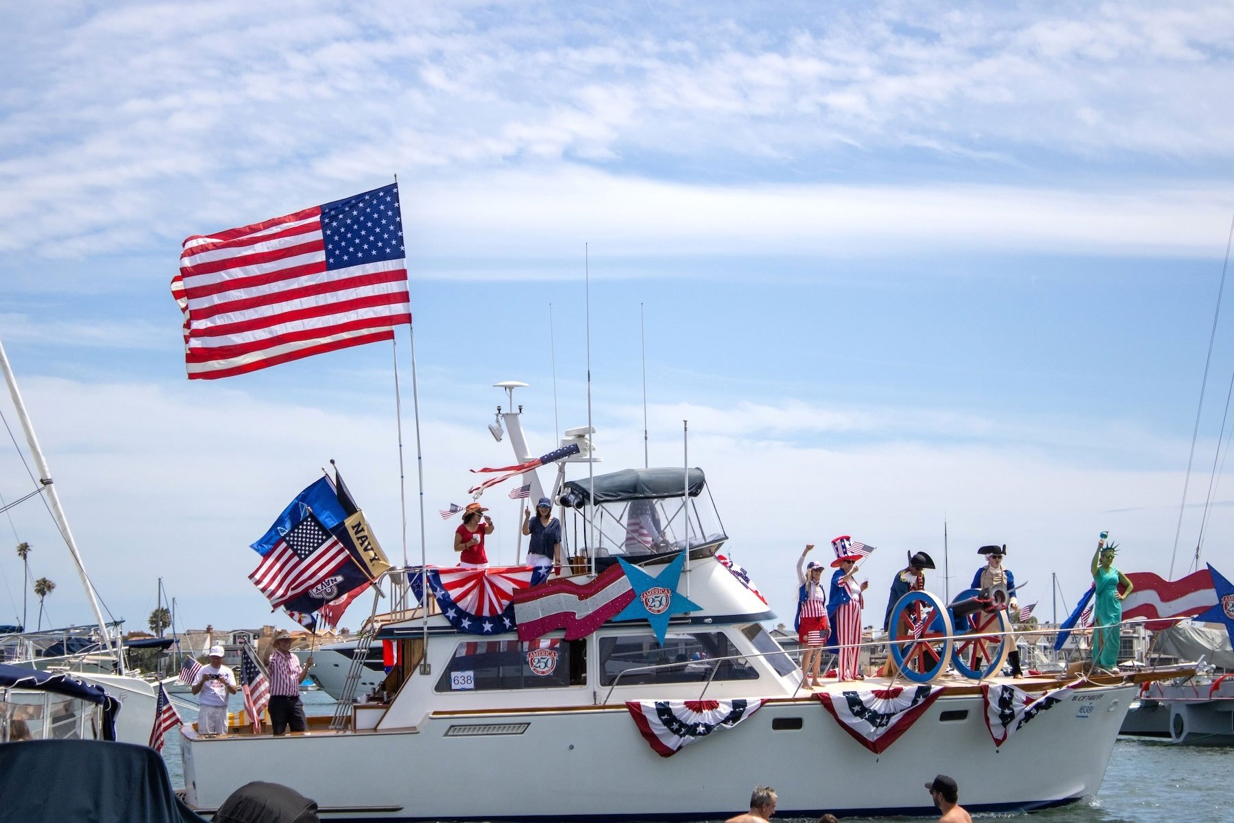 Decorated yacht with American flags and costumed passengers including a Statue of Liberty figure in a harbor.
