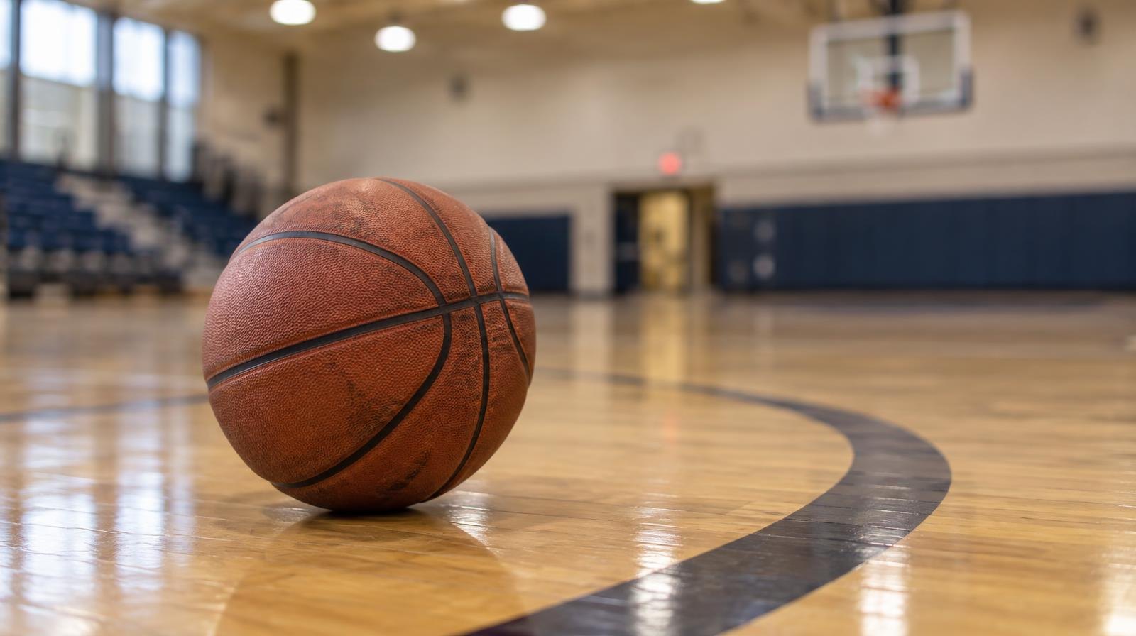 A basketball resting on a hardwood gymnasium floor near the three-point arc.