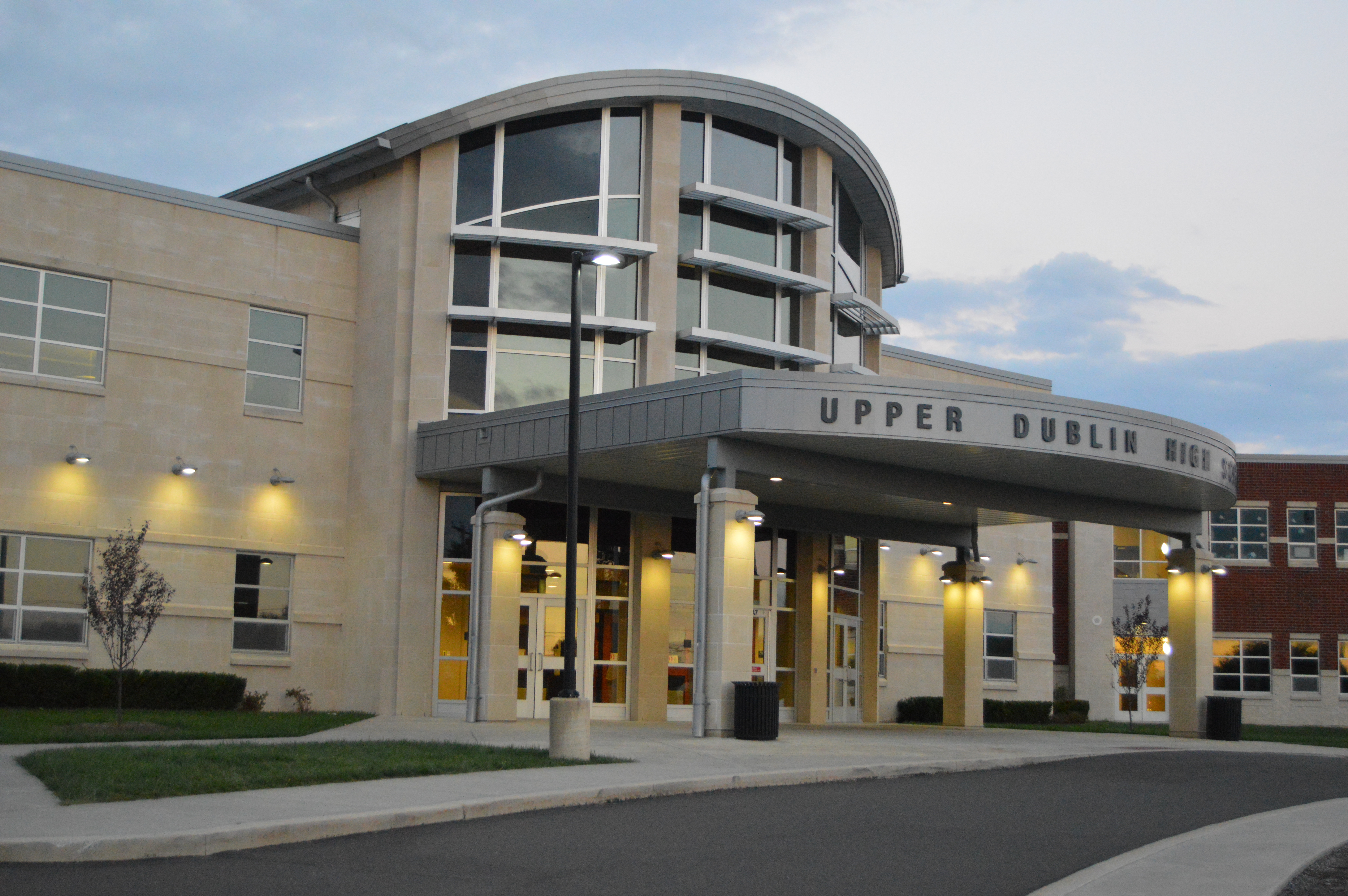 Illuminated entrance of a modern brick and glass high school building at dusk.