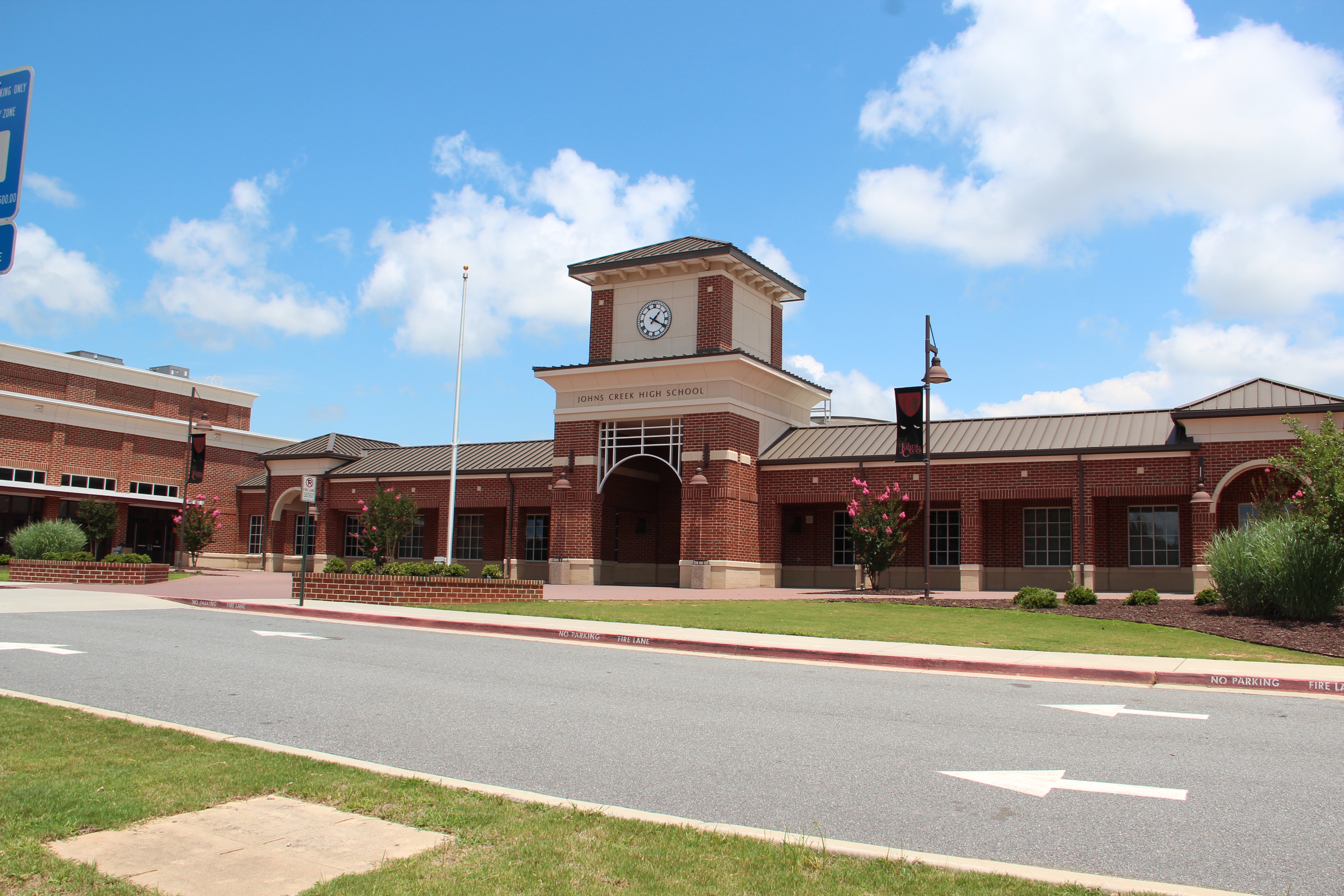 Brick school building with clock tower, arched entrance, and flagpole under partly cloudy sky.