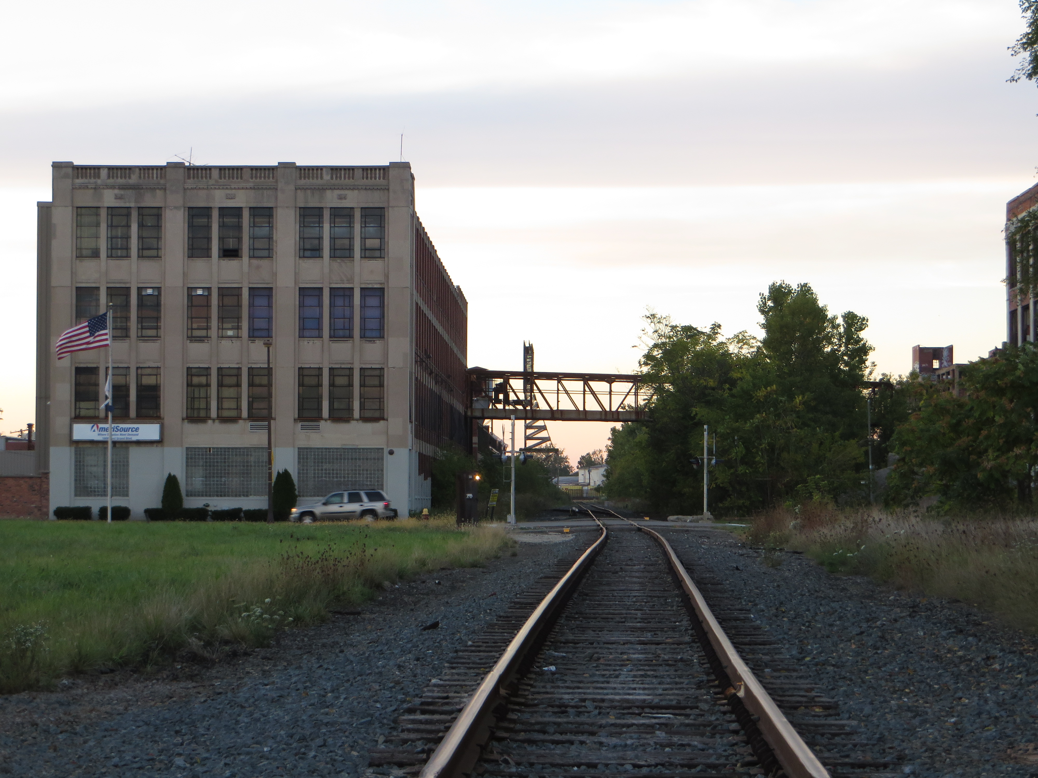 Large multi-story industrial brick building beside railroad tracks with an American flag on its facade.